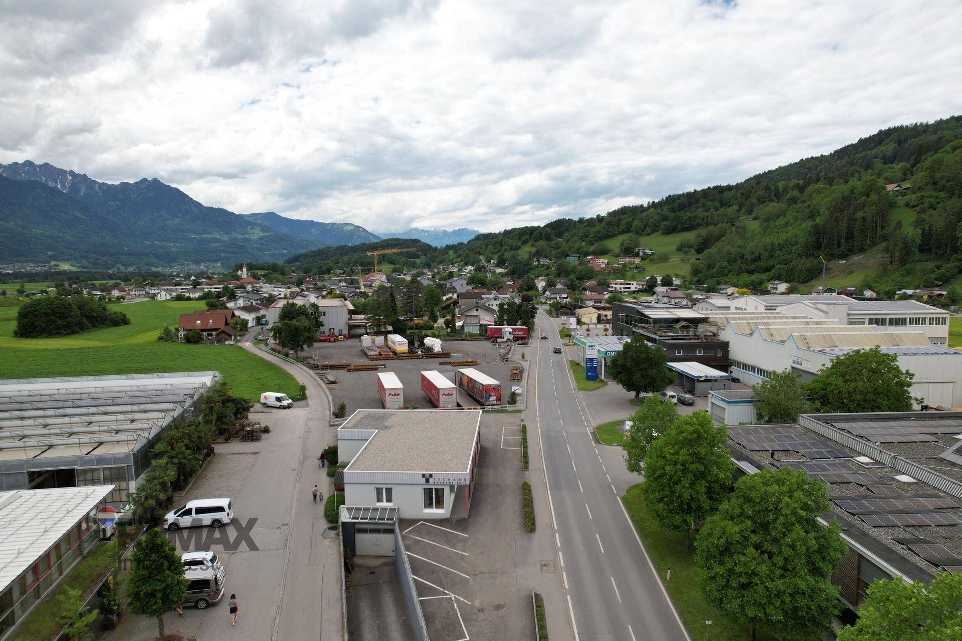 Weitläufige Luftaufnahme des Gewerbegebiets mit Straße, umliegender Bebauung und ländlicher Landschaft.