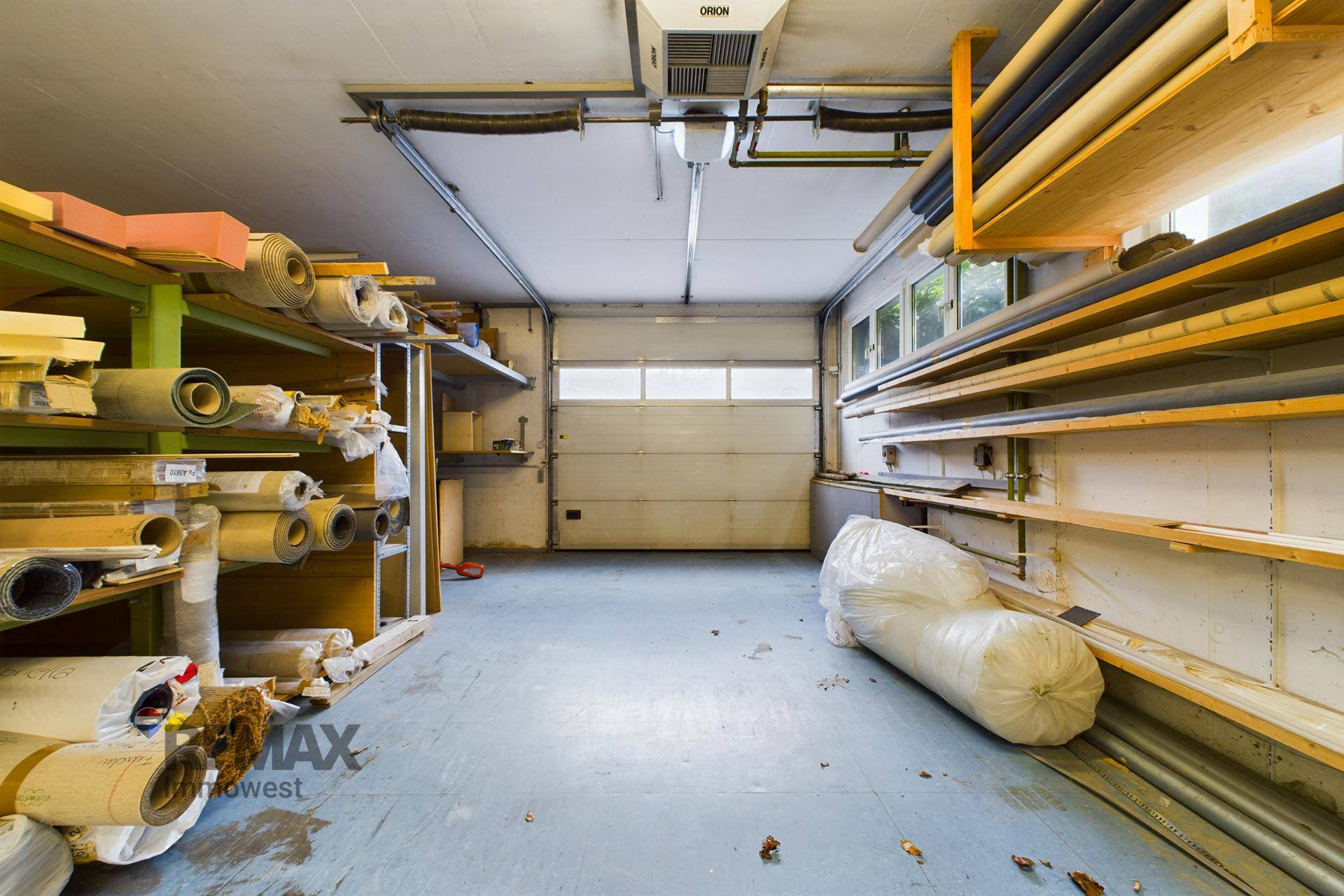 Geräumiger Lagerraum oder Werkstatt mit Regalen voller Rollenmaterialien und einem großen Garagentor.