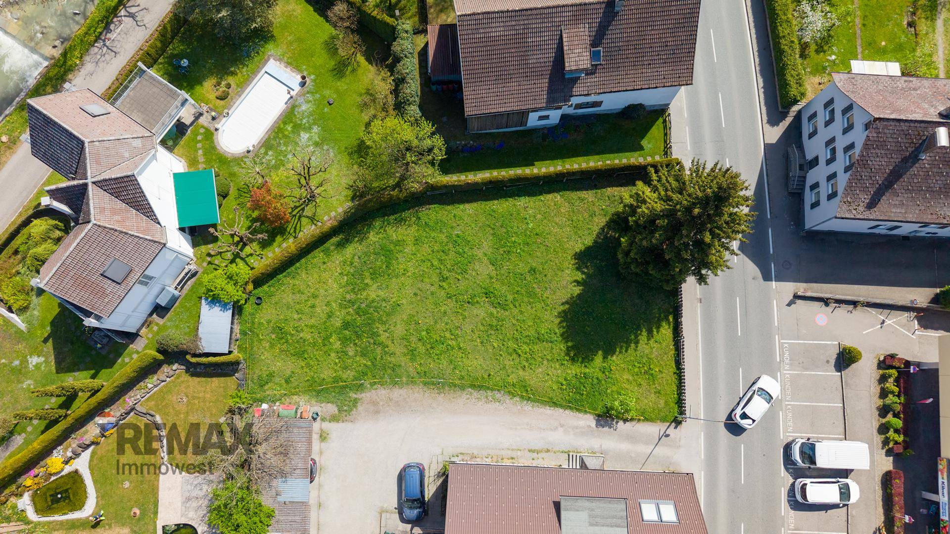 Luftaufnahme eines grünen Grundstücks mit angrenzenden Häusern, Straße und einem Pool in der Nachbarschaft.