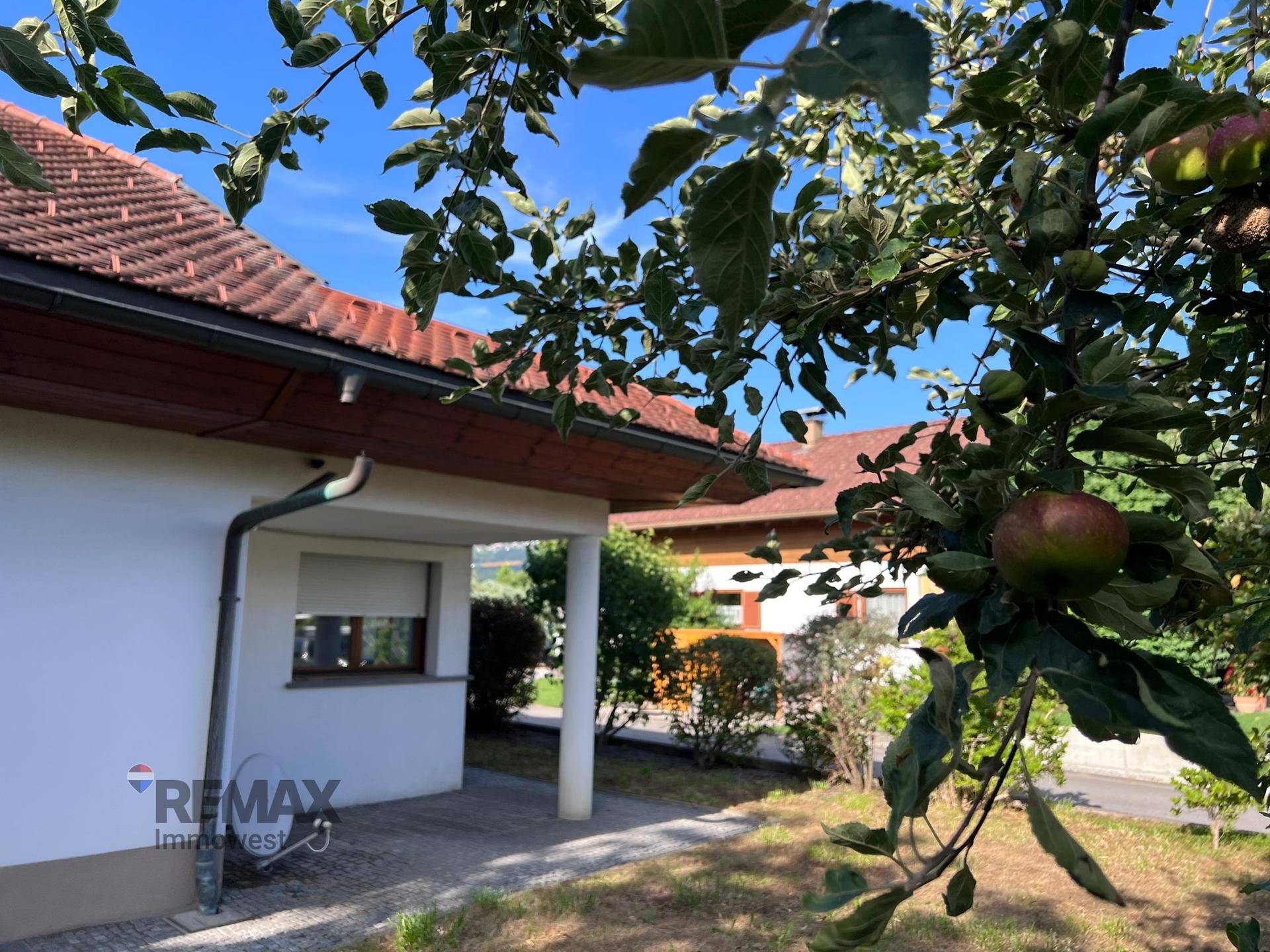 Seitenansicht des Hauses mit Dachüberstand und grüner Umgebung unter klarem Himmel.