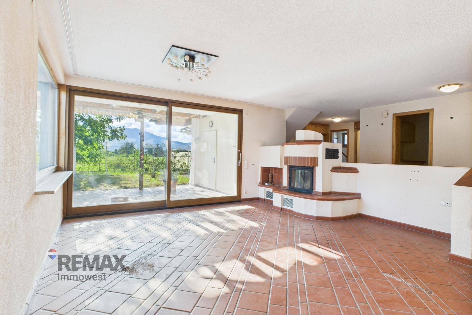 Geräumiges Wohnzimmer mit Kachelofen, großen Schiebetüren und Bergblick zur Terrasse.