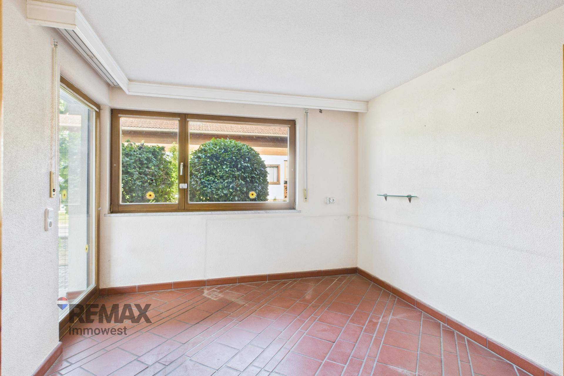 Leerer Raum mit Terrakottafliesen und großem Fenster, das viel Tageslicht hereinlässt.