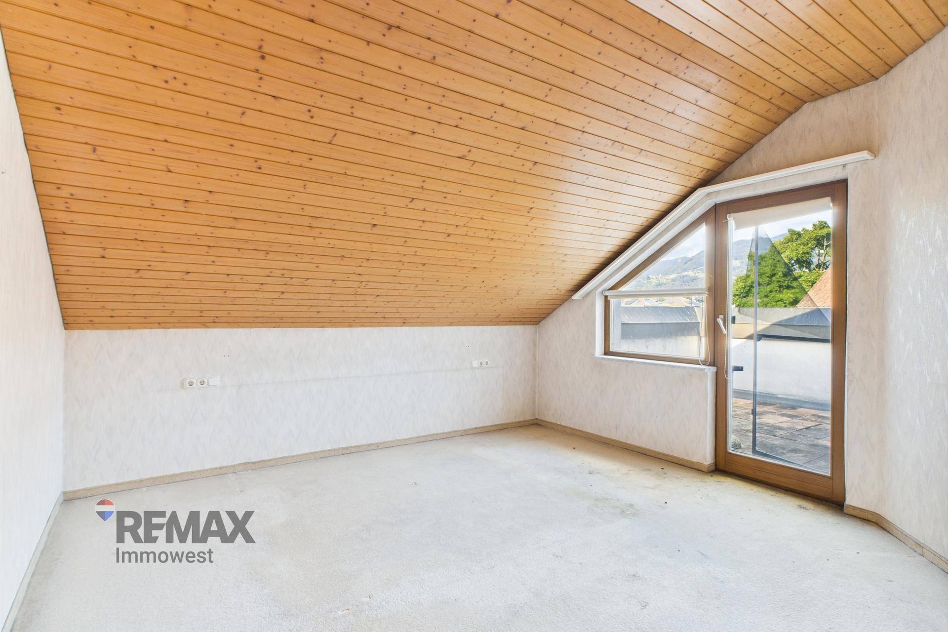 Dachzimmer mit Holzverkleidung an der Decke und Zugang zu einer Dachterrasse.