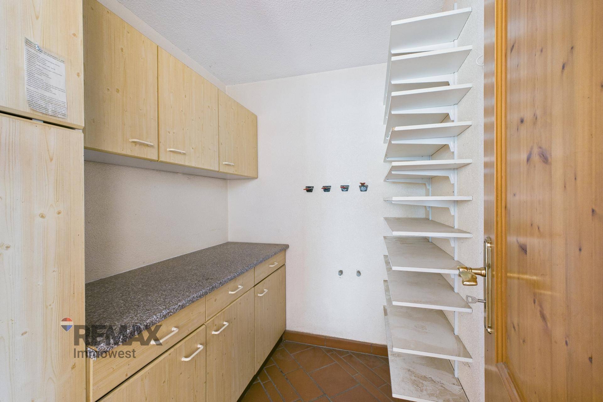 Praktischer Hauswirtschaftsraum mit Holzschränken, Arbeitsplatte und offenen Regalen.