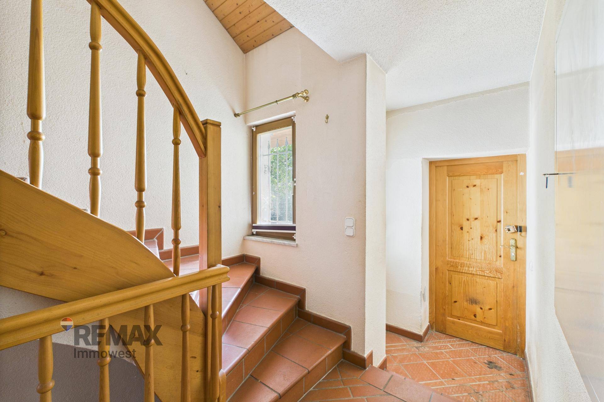 Treppenabsatz mit Fenster und Holztür, der zu weiteren Räumen führt.