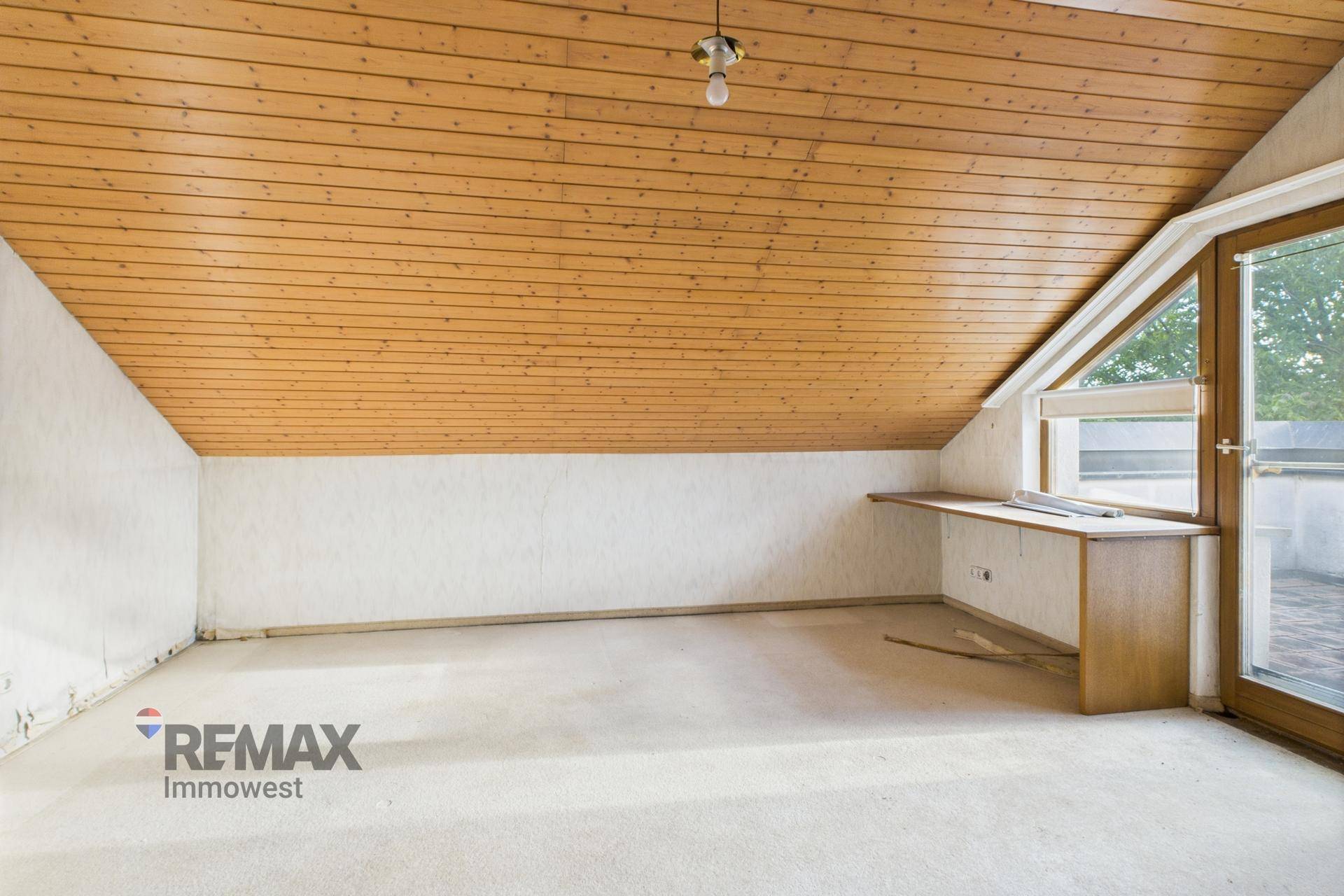 Helles Dachzimmer mit Holzdeckenverkleidung, Teppichboden und Zugang zu einer kleinen Terrasse.