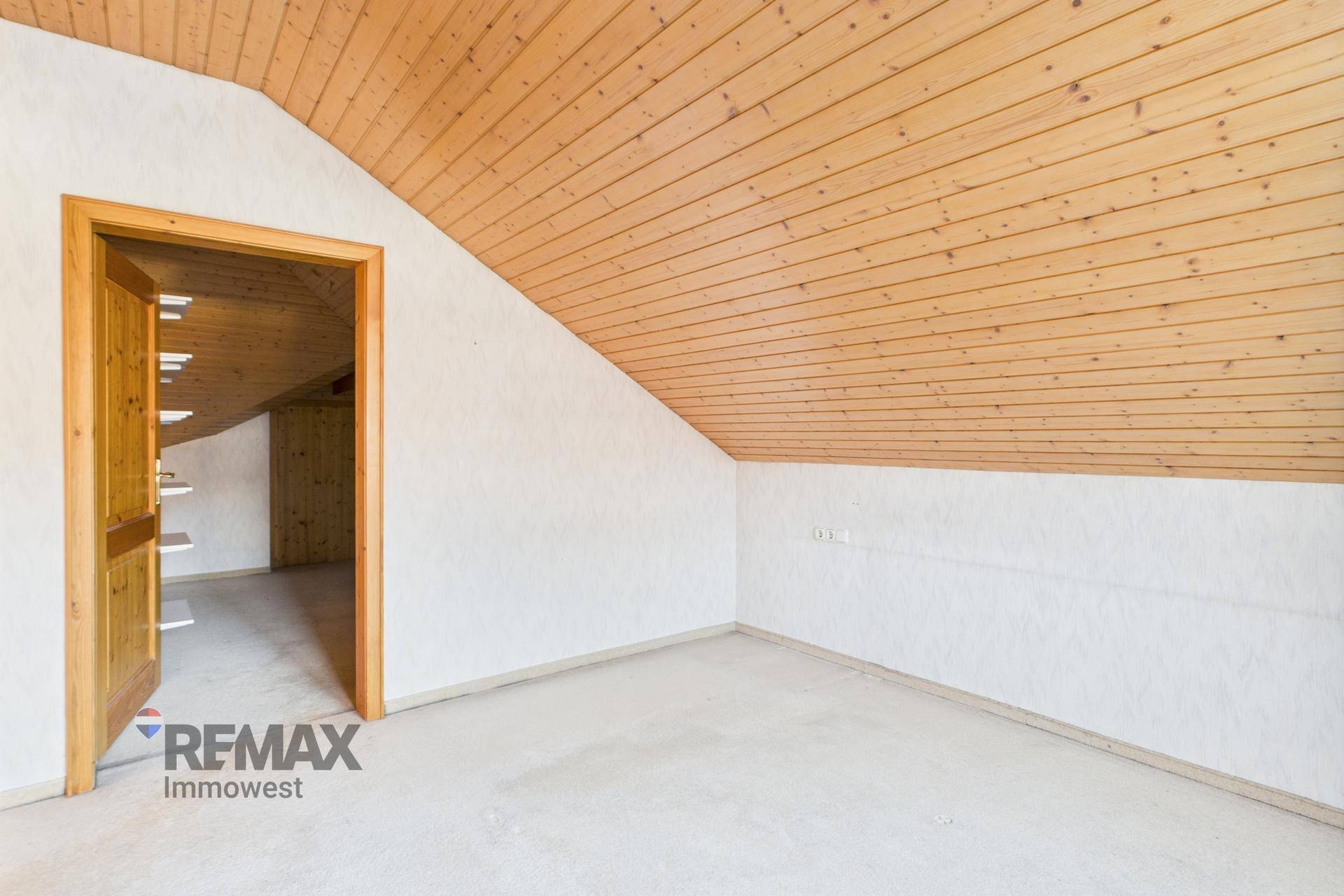 Geräumiges Dachzimmer mit Holzdecke und Holztür, bereit zur individuellen Gestaltung und Nutzung.