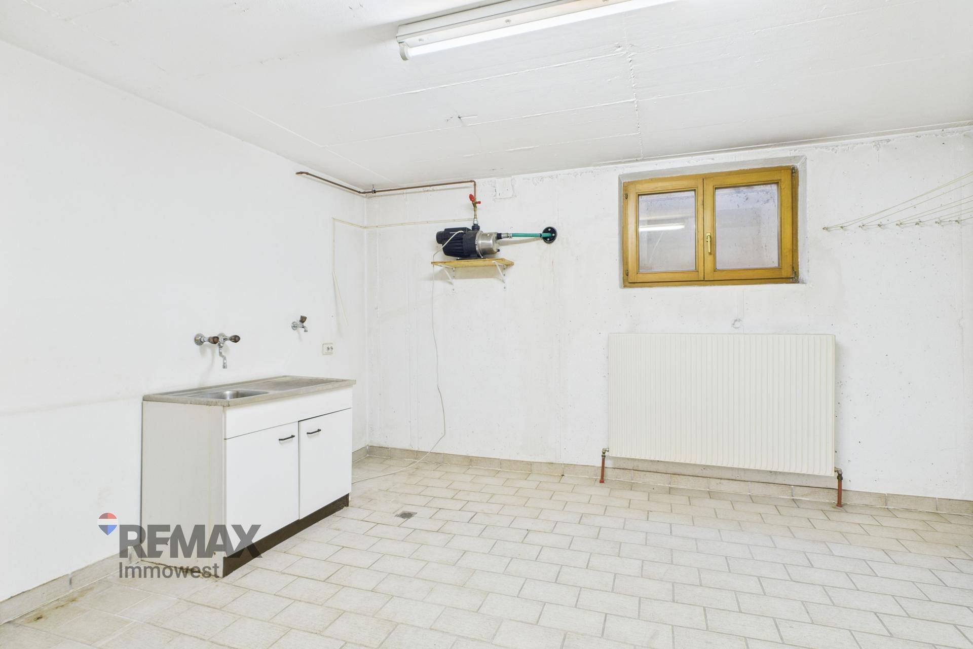Waschküche im Keller mit Waschbecken, Heizkörper und Fenster für Belüftung und Tageslicht.