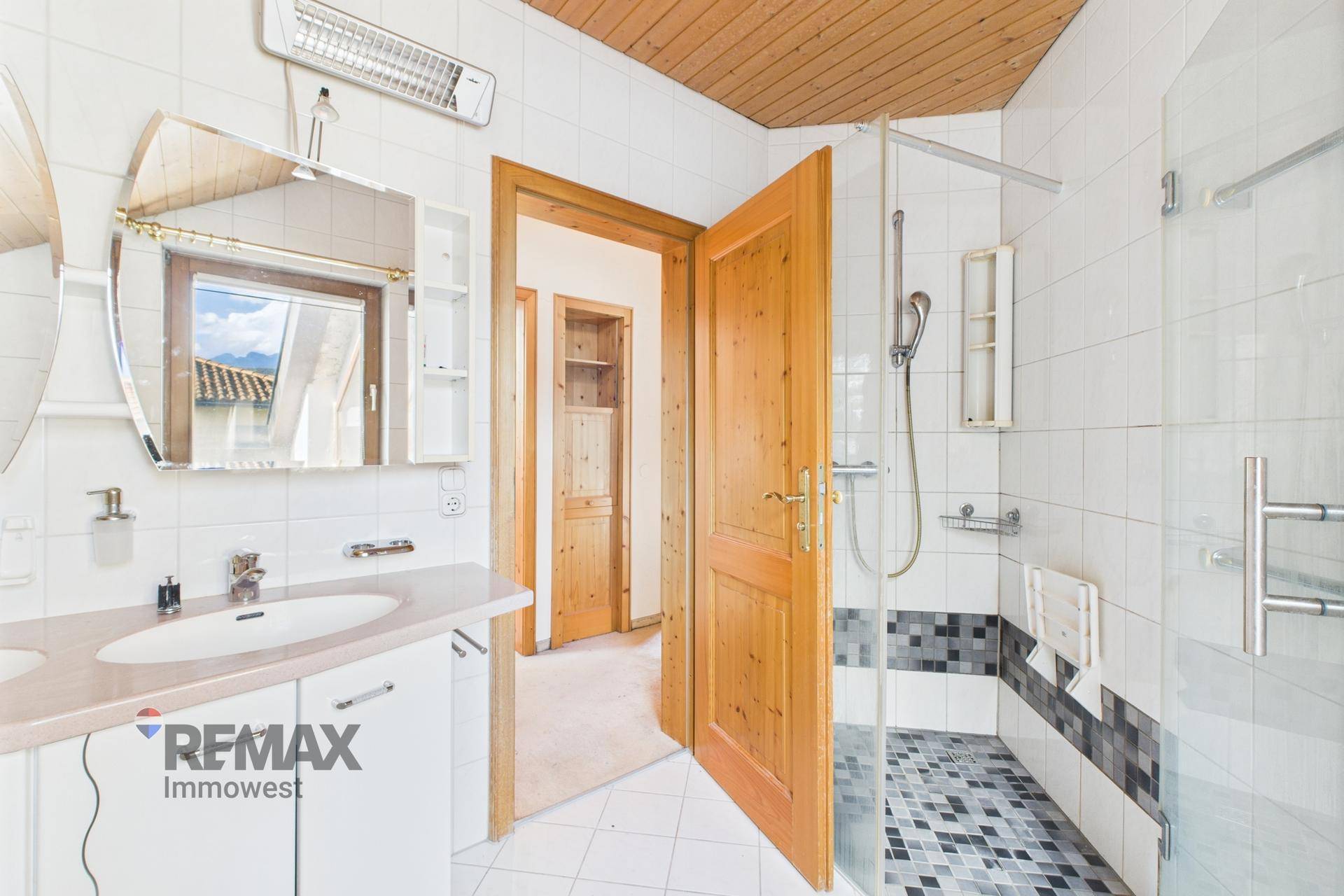Helles Badezimmer mit Duschkabine, Doppelwaschbecken und Dachfenster für natürliches Tageslicht.
