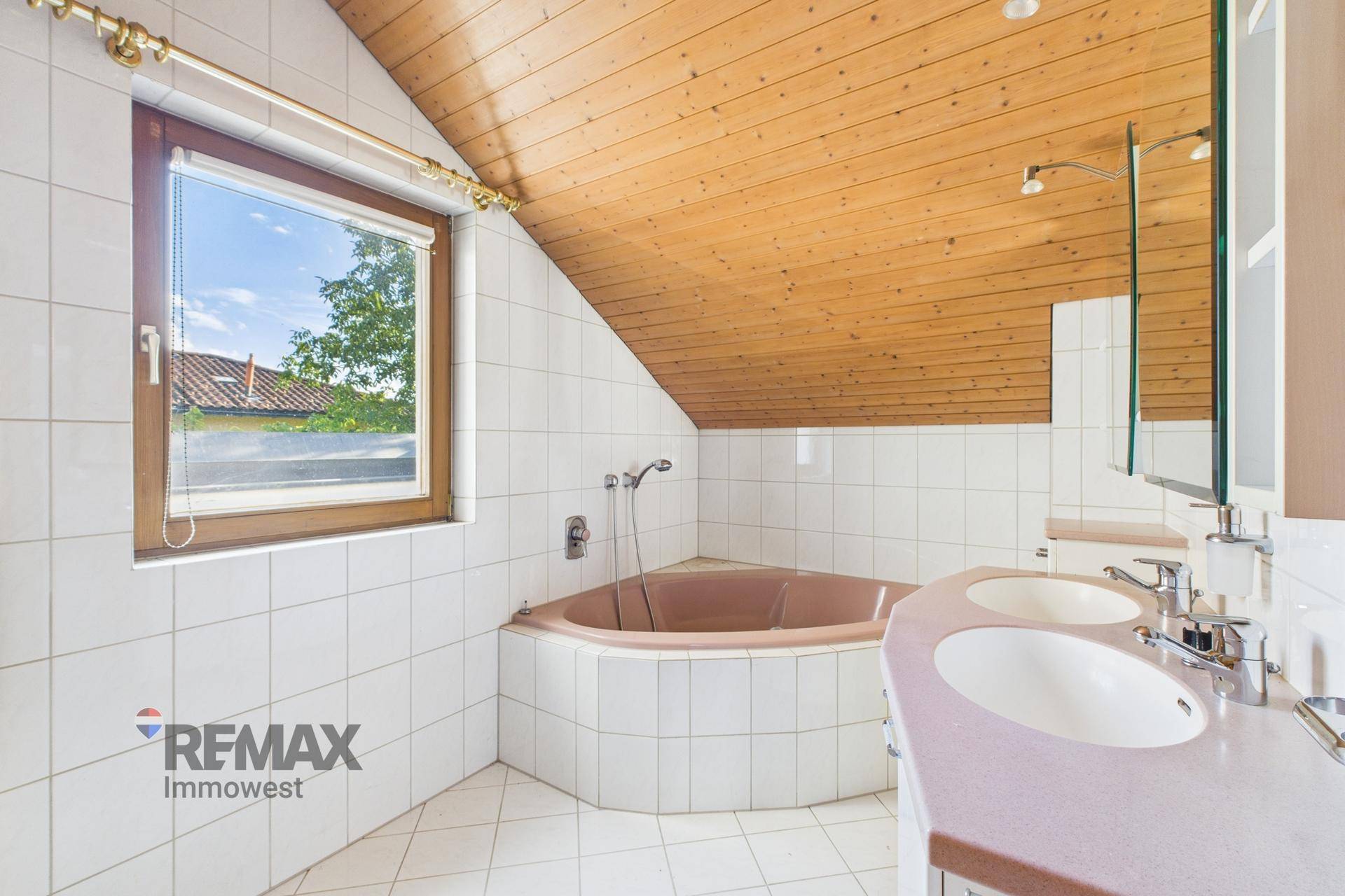 Badezimmer im Dachgeschoss mit Eckbadewanne, Doppelwaschbecken und Holzdeckenverkleidung im 80er-Jahre-Stil.