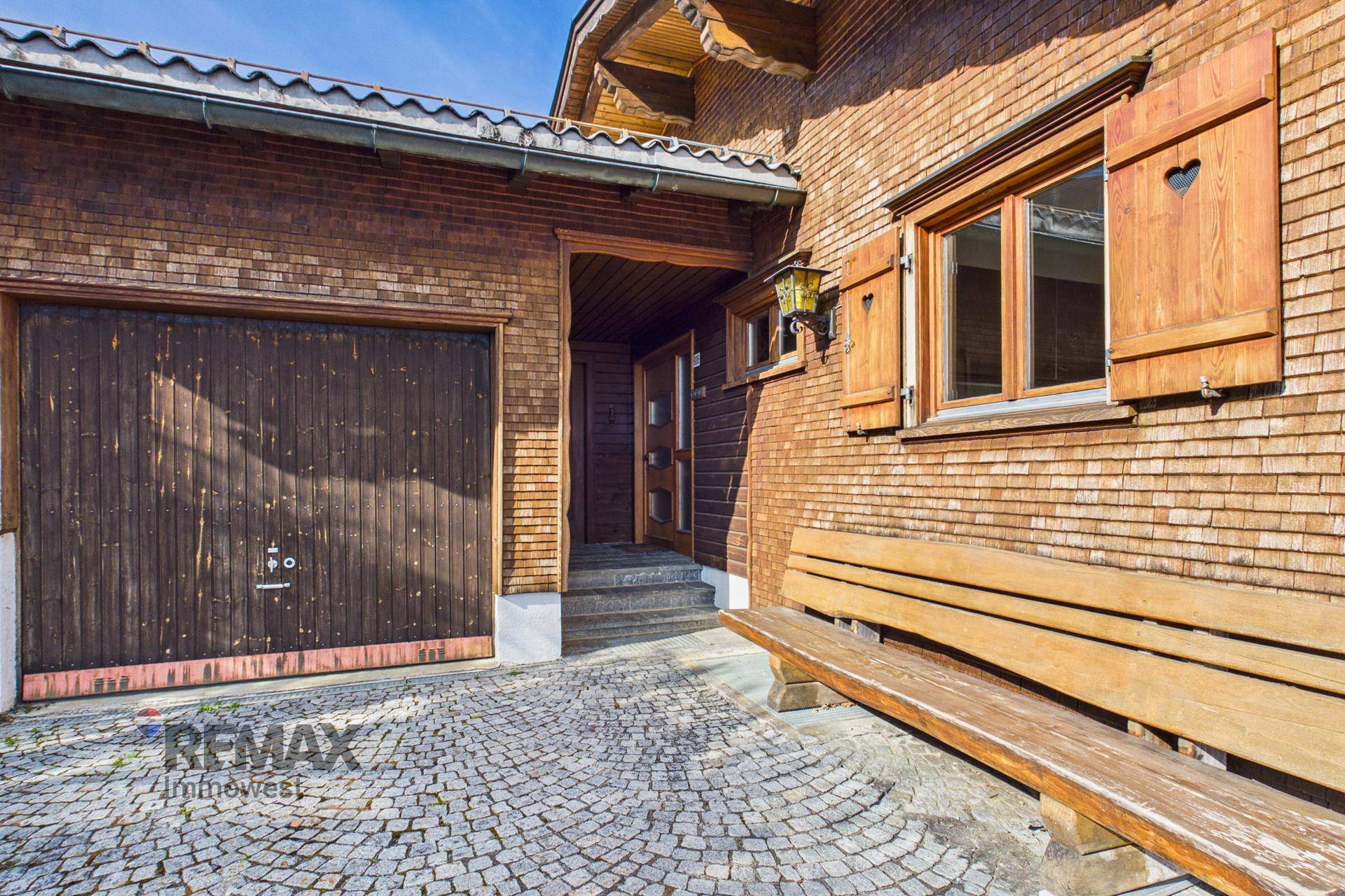 Eingangsbereich des Holzhauses mit Garage, Holztür und rustikaler Sitzbank.