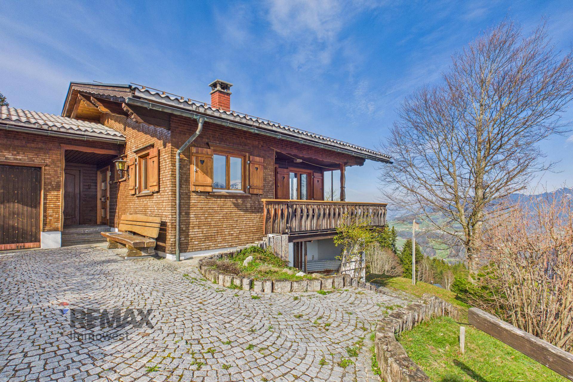 Charmantes Holzhaus im Chalet-Stil mit gepflastertem Vorplatz und weitem Bergblick.