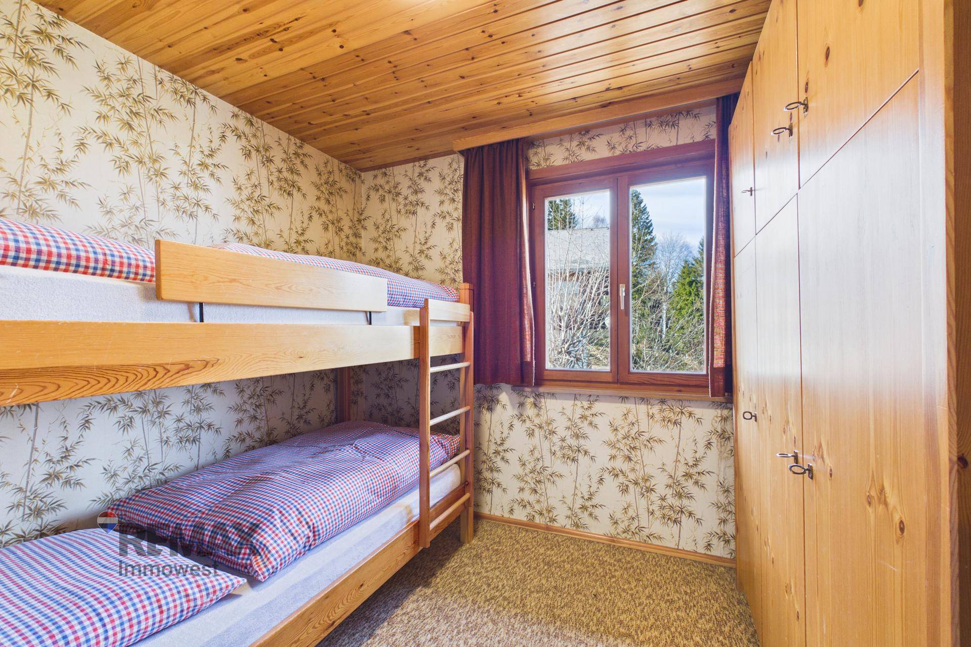 Kinderzimmer mit Etagenbett, Holzschrank und gemusterter Tapete.