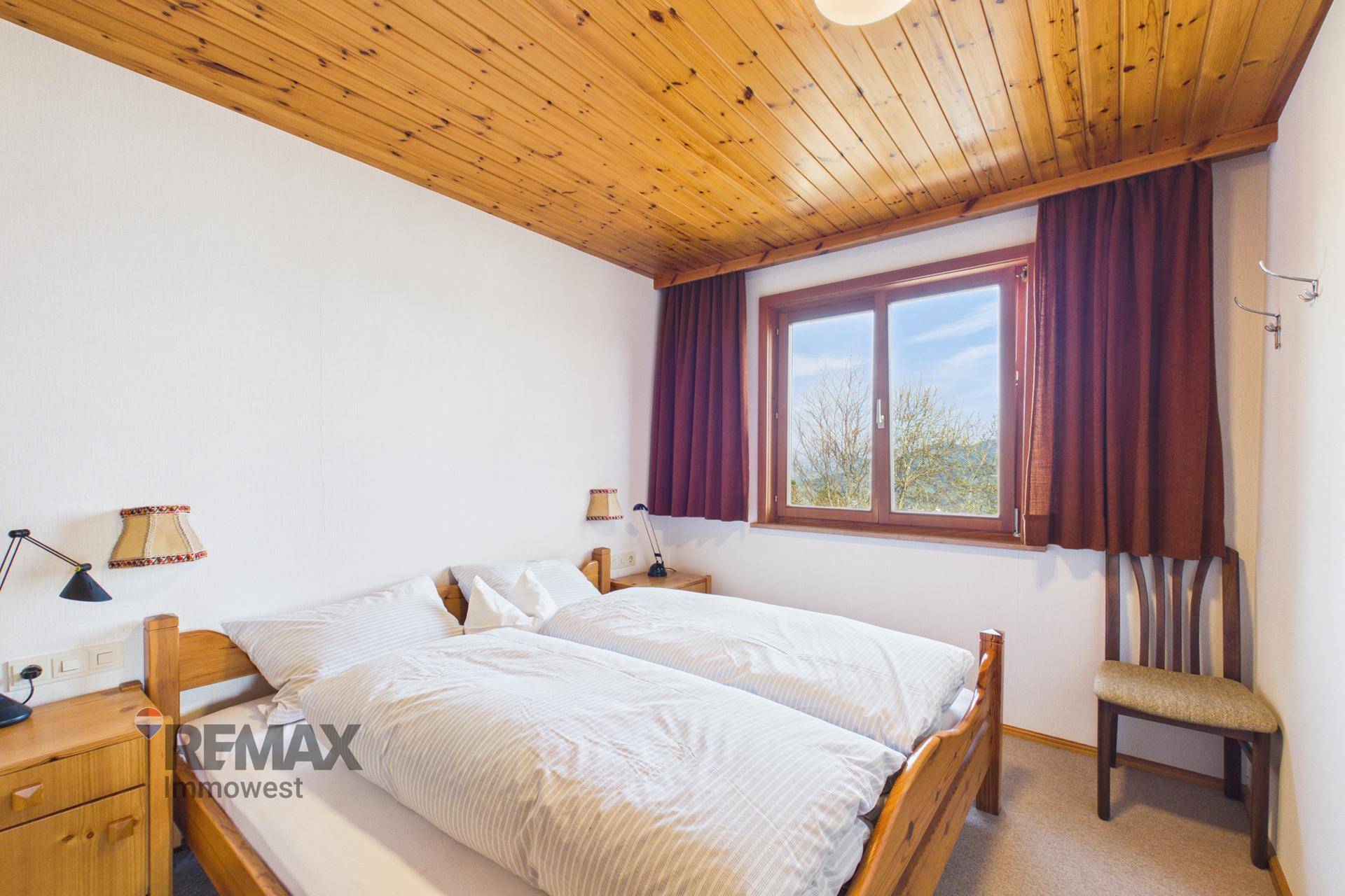 Helles Schlafzimmer mit zwei Einzelbetten, Holzdecke und großem Fenster.