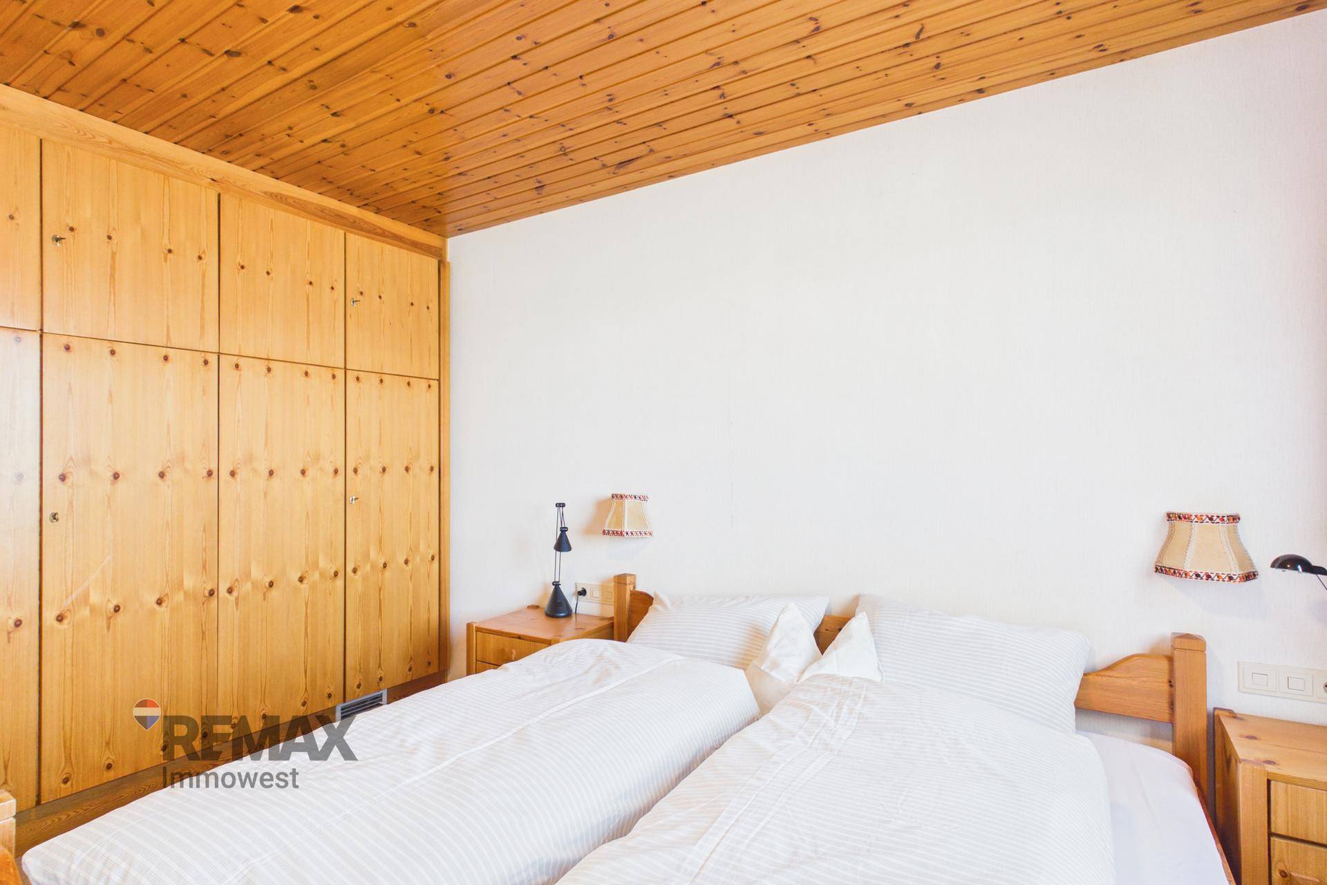 Schlafzimmer mit Holzschrank, zwei Einzelbetten und Holzdecke.