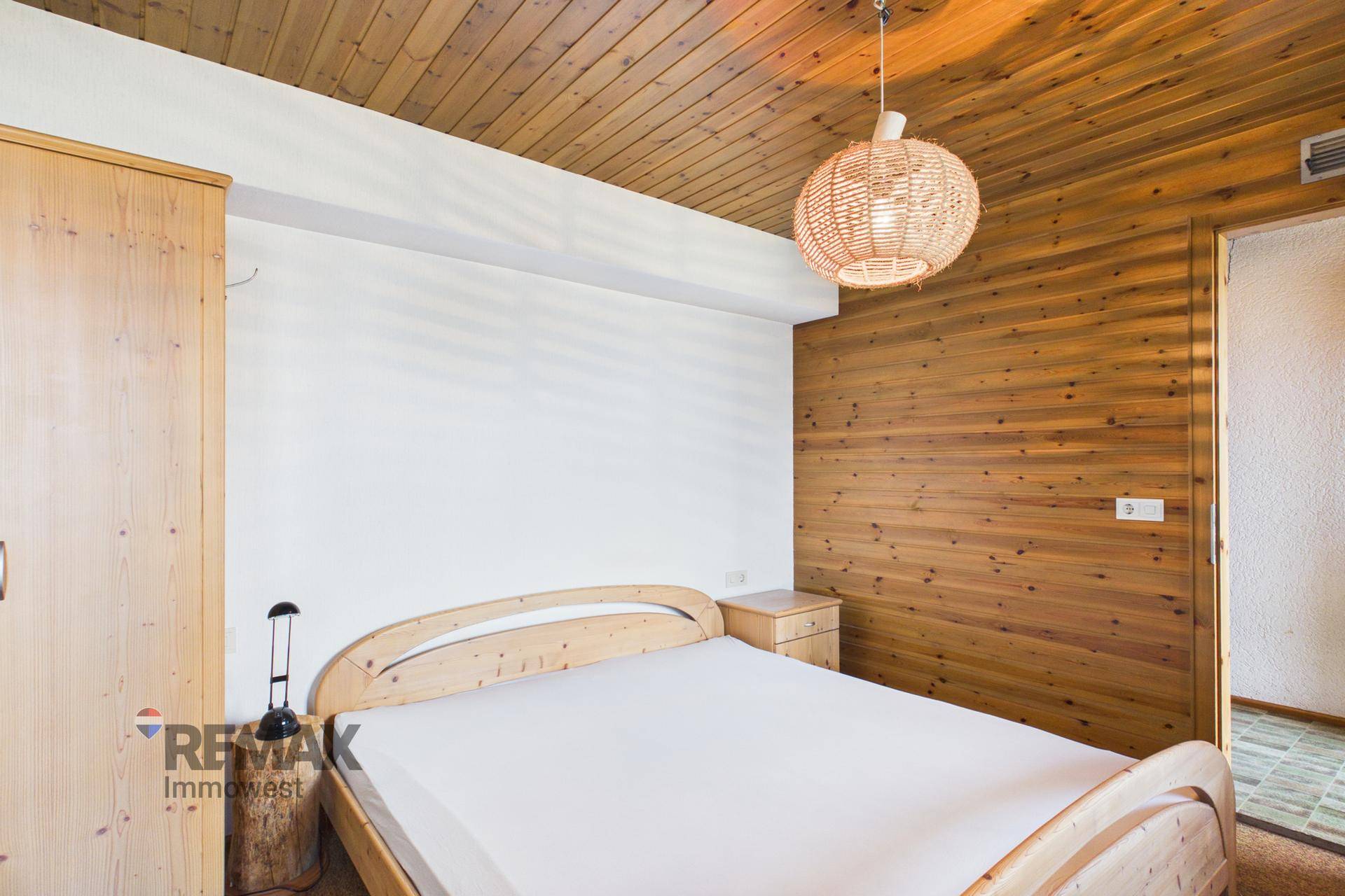 Schlafzimmer mit Einzelbett, Holzvertäfelung und schlichter Einrichtung.