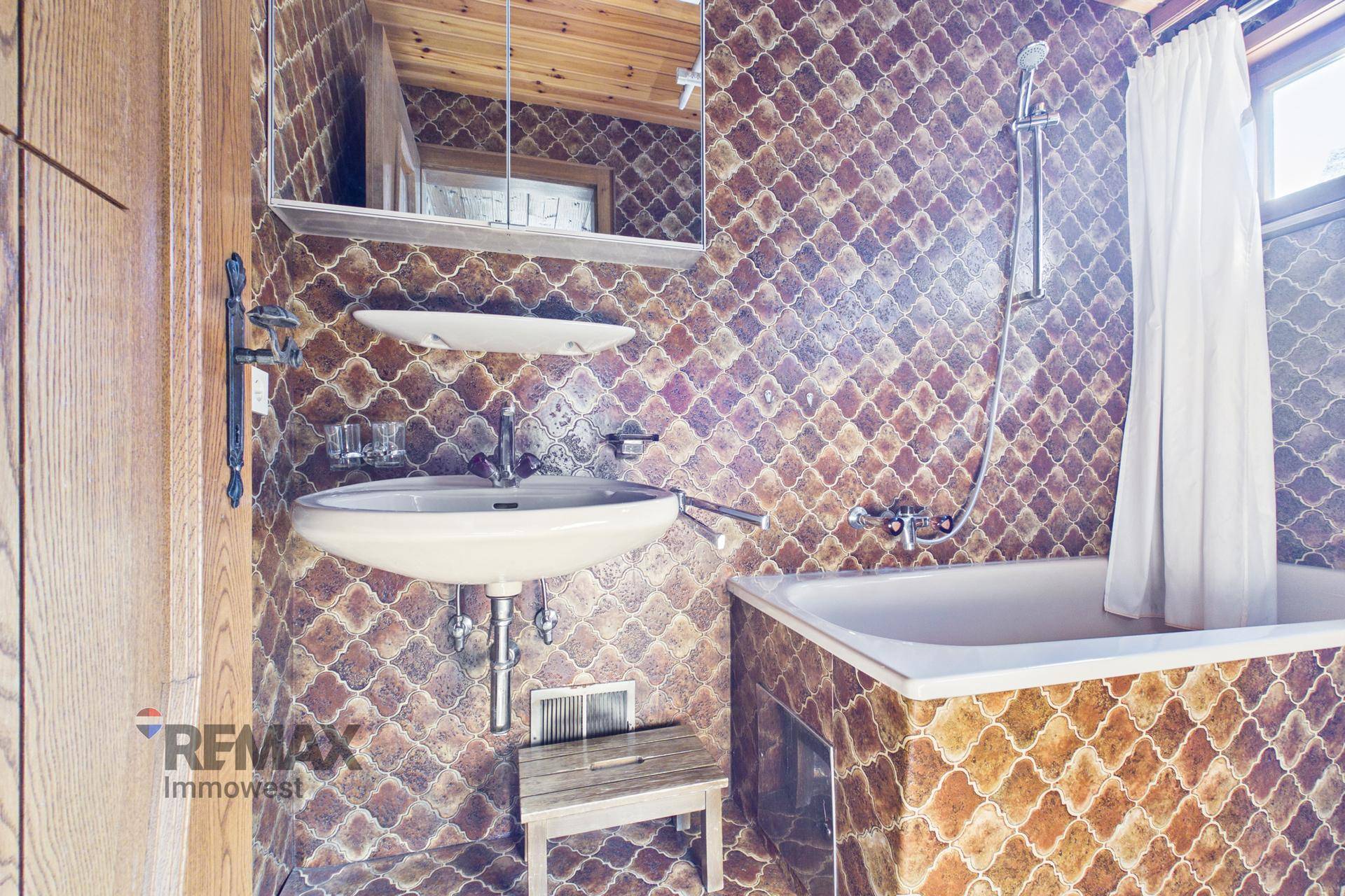 Badezimmer mit Badewanne, Waschbecken und gemusterten Fliesen im 80er-Jahre-Stil.