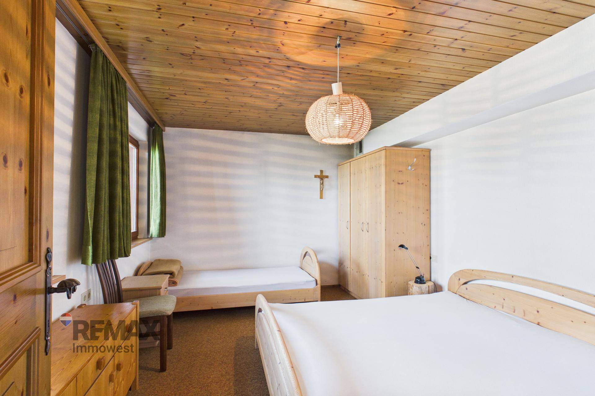 Helles Schlafzimmer mit zwei Einzelbetten, Holzdecke und Fenster mit grüner Aussicht.