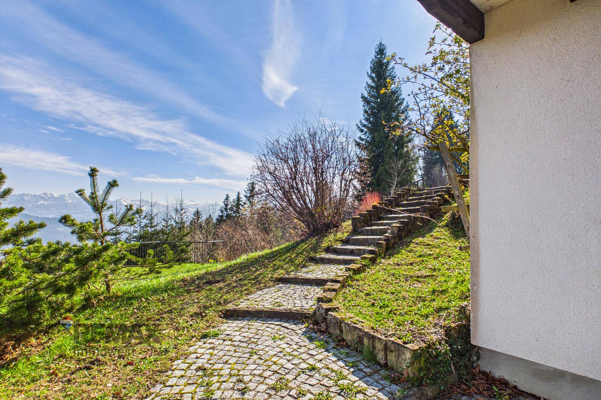Steintreppe im Gartenbereich mit gepflastertem Weg und Blick auf die Berge.