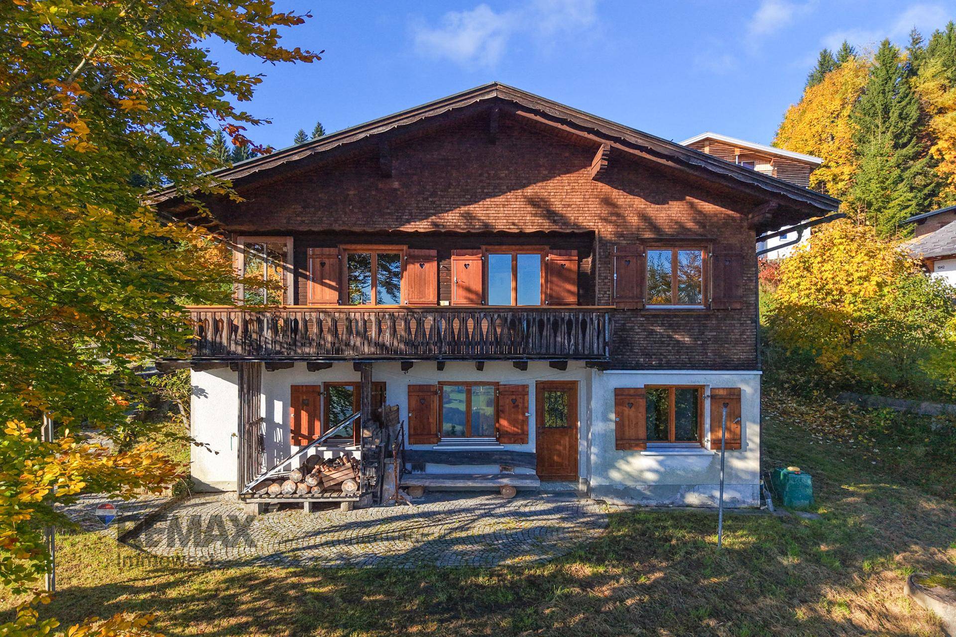 Charmantes Holzhaus im Chalet-Stil mit Balkon und herbstlicher Umgebung.