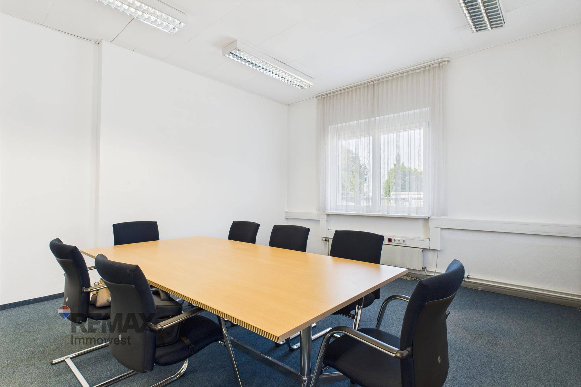 Besprechungsraum mit großem Holztisch und schwarzen Bürostühlen, beleuchtet durch ein Fenster.