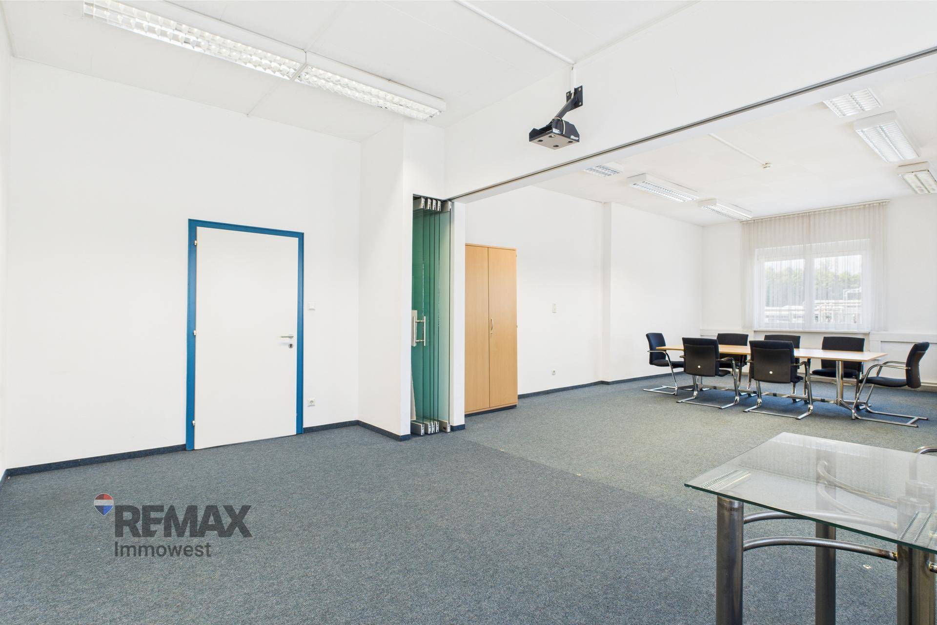 Konferenzraum mit blauem Teppichboden, weißer Tür mit blauer Zarge und einem Beamer an der Decke.