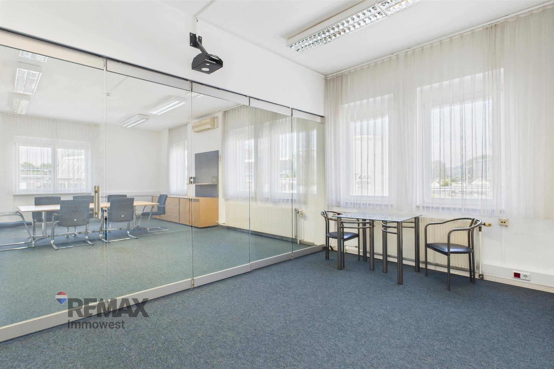 Konferenzraum mit Glastrennwand, die den Raum unterteilt, und einem Beamer an der Decke.
