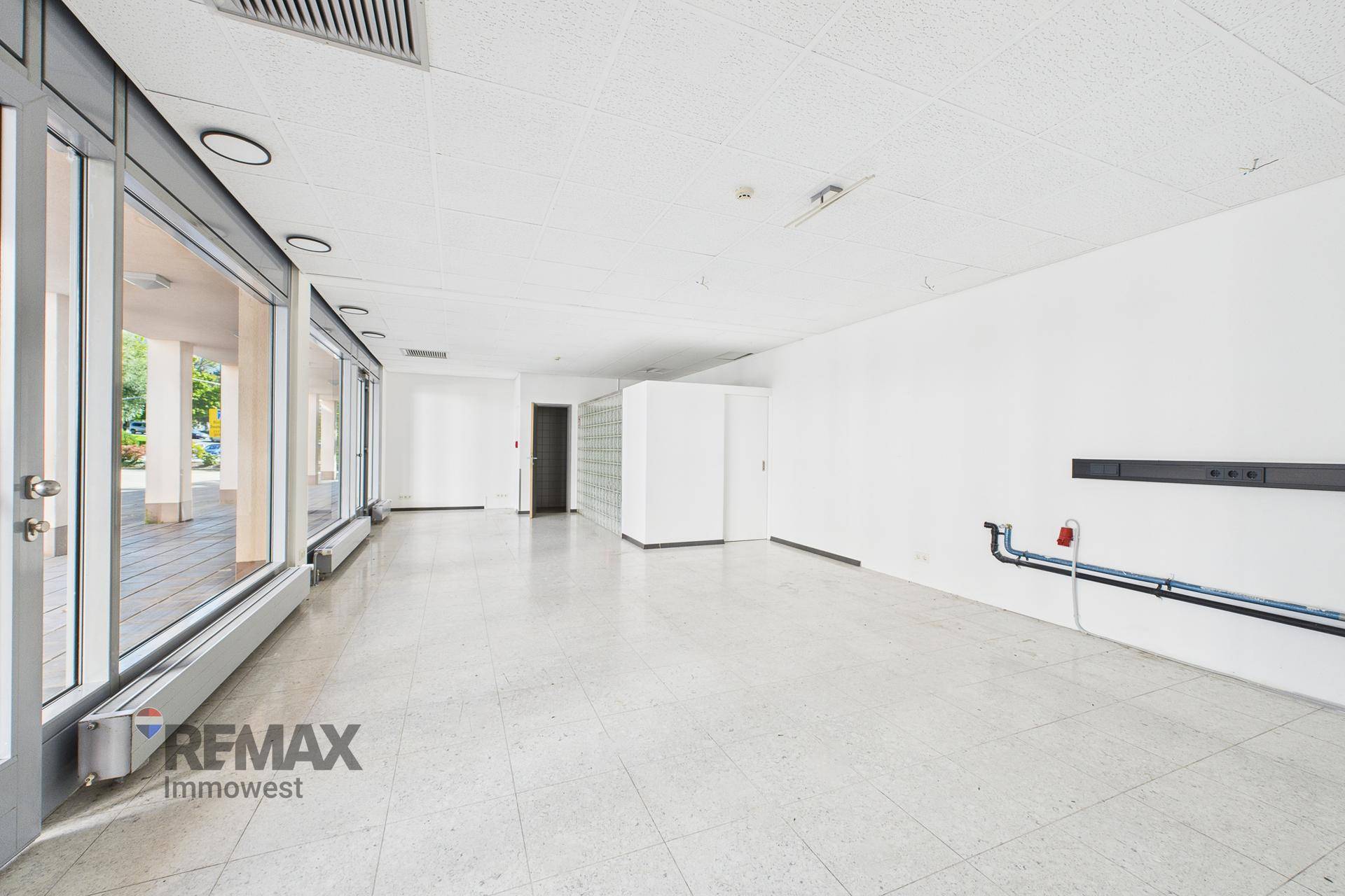 Großer, leerer Gewerberaum mit Fliesenboden, großen Fenstern und abgehängter Decke.