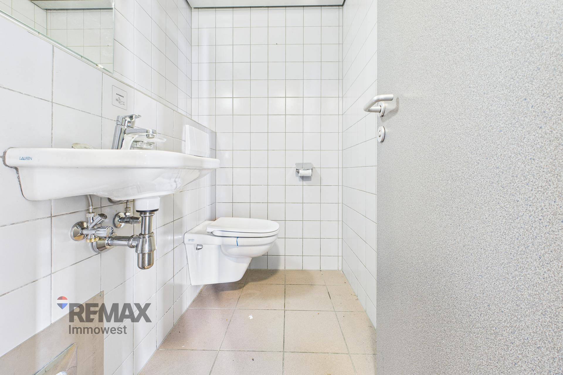 Einfache Toilette mit weißen Wandfliesen, Waschbecken und wandhängendem WC.