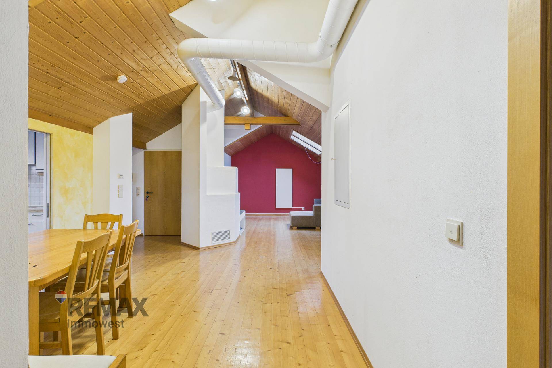 Geräumiger Wohn- und Essbereich mit durchgehendem Holzboden und sichtbaren Holzbalken an der Decke.