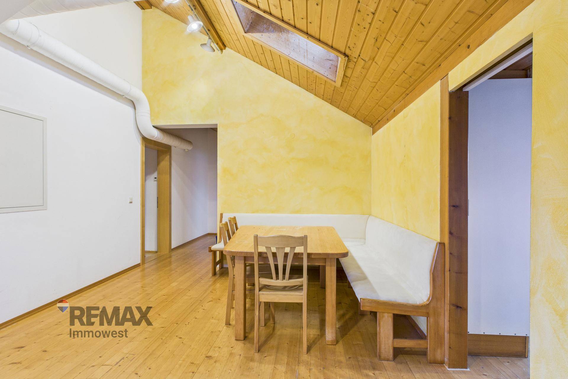 Heller Essbereich mit Holztisch und Sitzbank, gelber Wand und Holzboden unter einem Dachfenster.