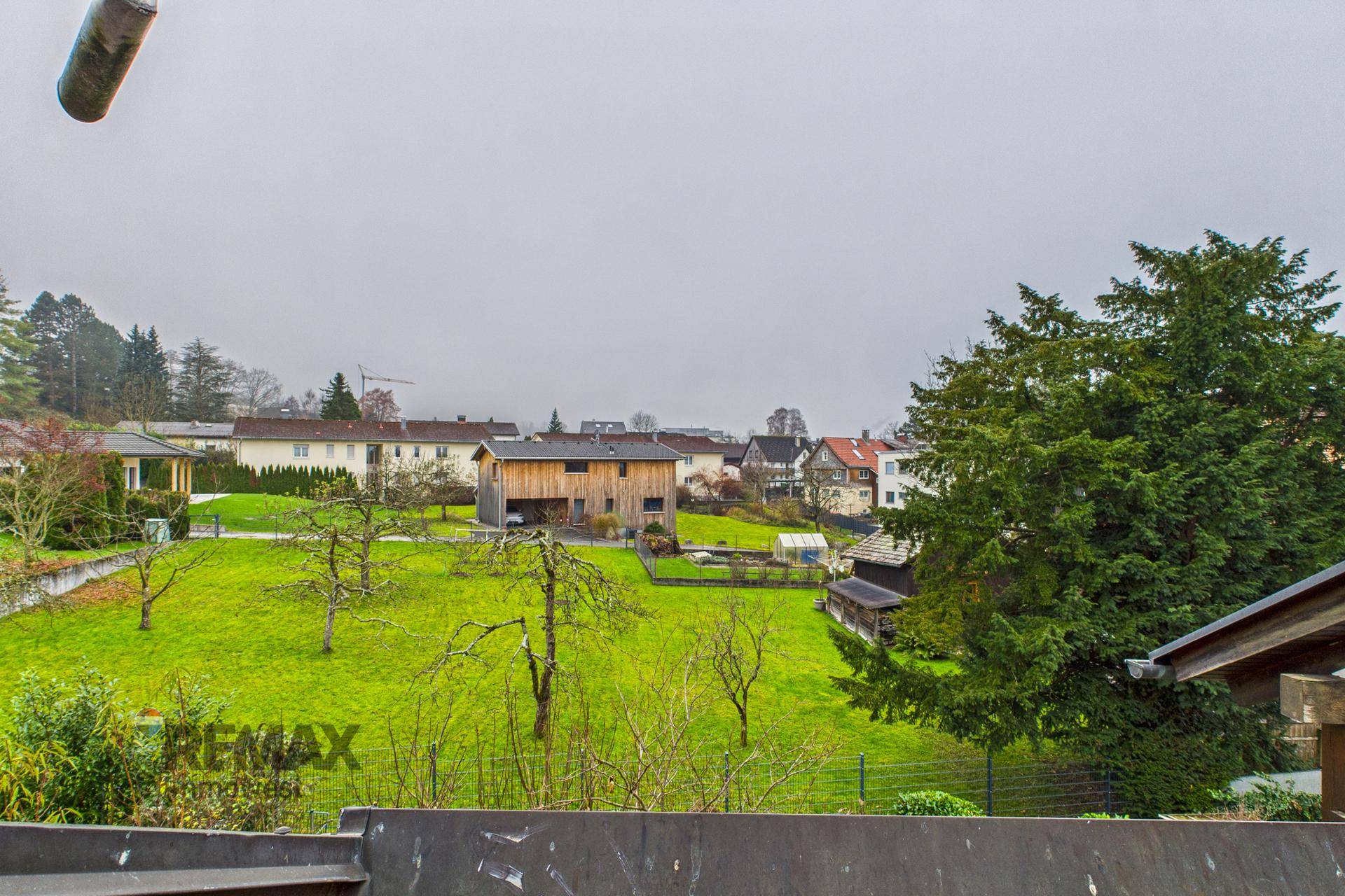 Panoramablick vom Balkon über eine weitläufige grüne Wiese mit Bäumen und Häusern in der Ferne.