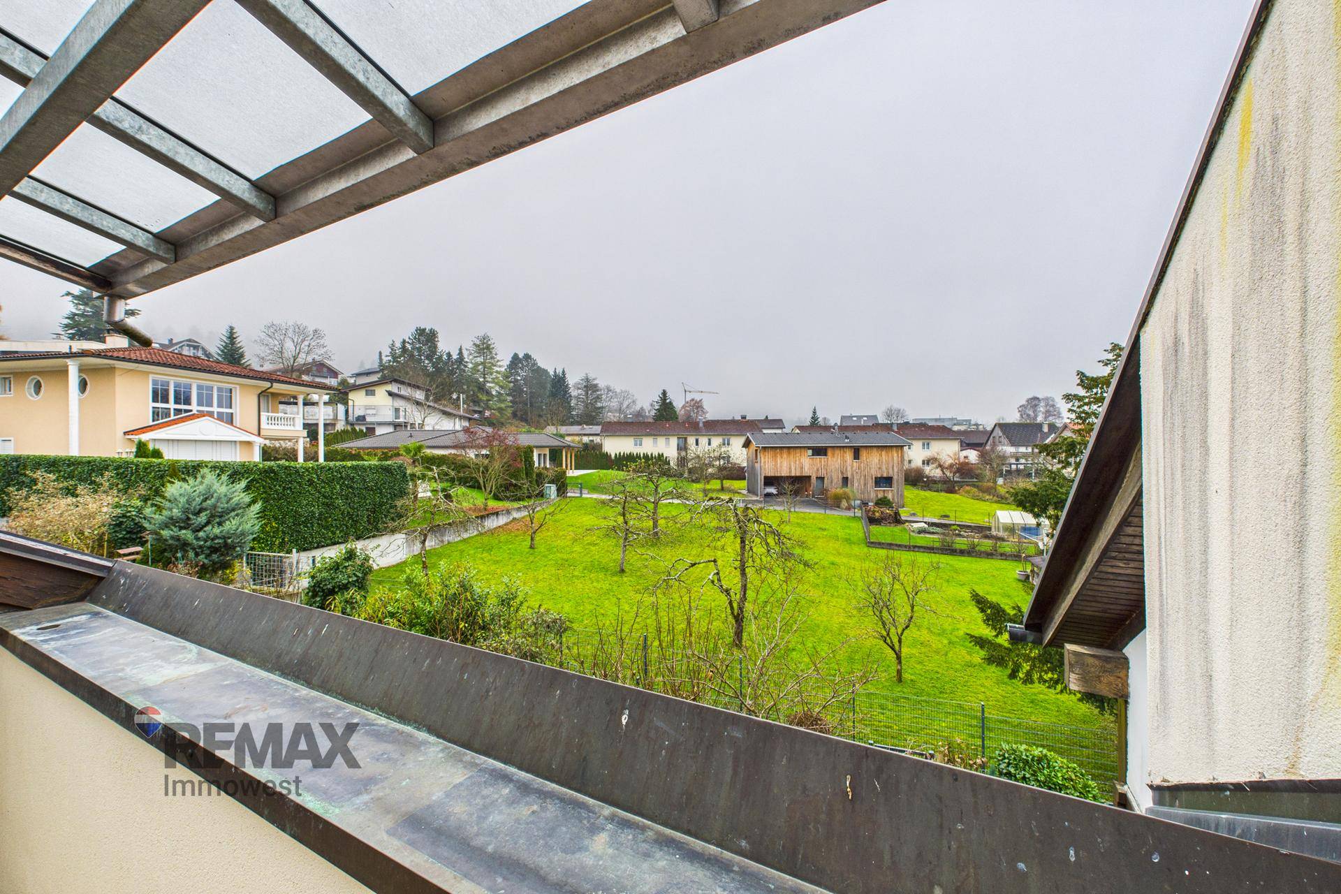 Weitläufiger Blick vom Balkon auf eine grüne Gartenlandschaft mit Bäumen und umliegenden Häusern.