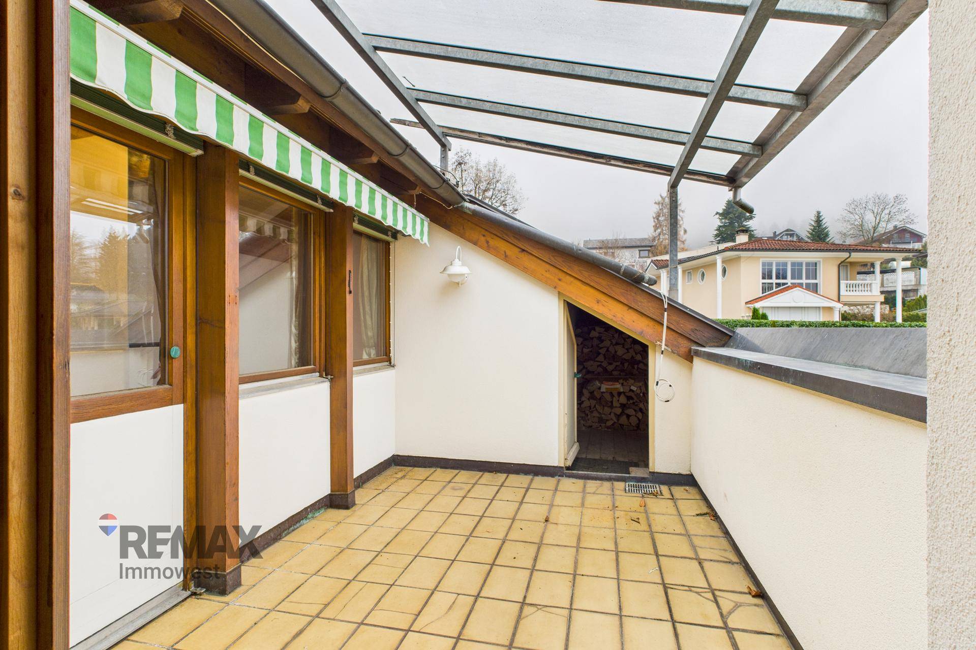 Überdachter Balkon mit gelben Fliesen und Stauraum für Holz, ideal für entspannte Stunden im Freien.