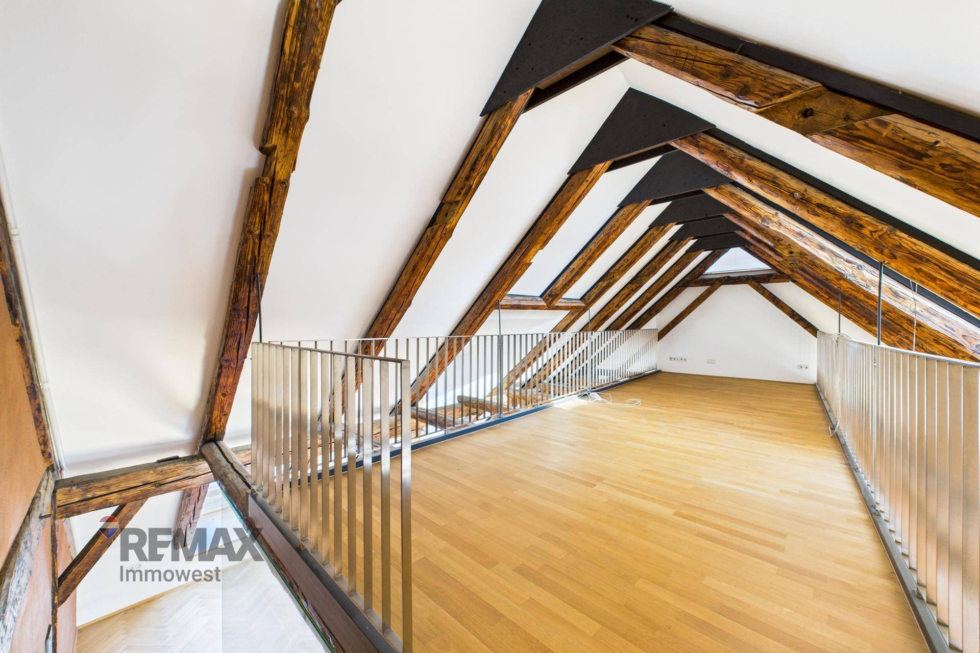 Helle Galerie im Dachgeschoss mit Holzbalken, schrägen Wänden und Metallgeländer.