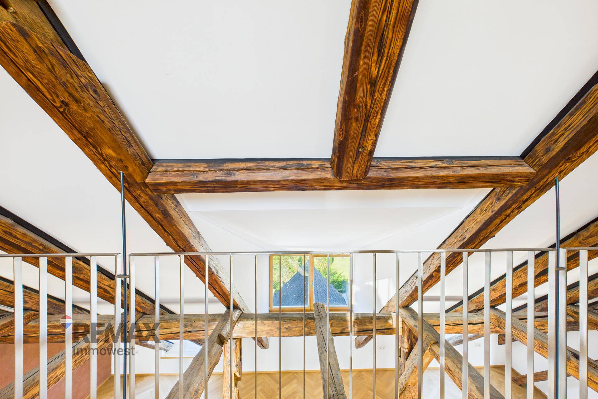 Blick von der oberen Galerie auf die untere Ebene mit Holzbalken und Dachfenster.