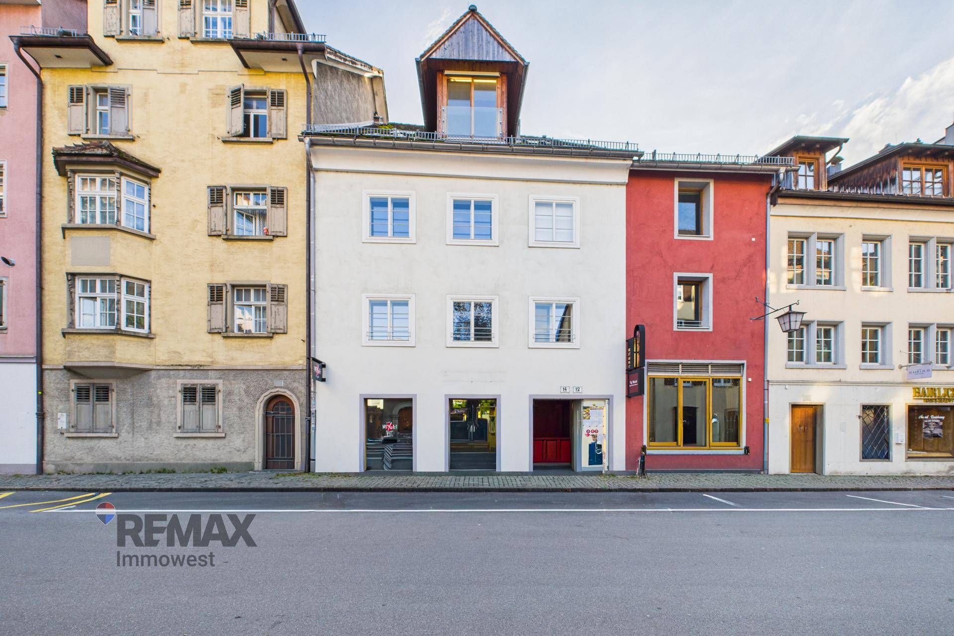 Historische Fassade des Gebäudes mit mehreren Fenstern und Geschäften im Erdgeschoss.