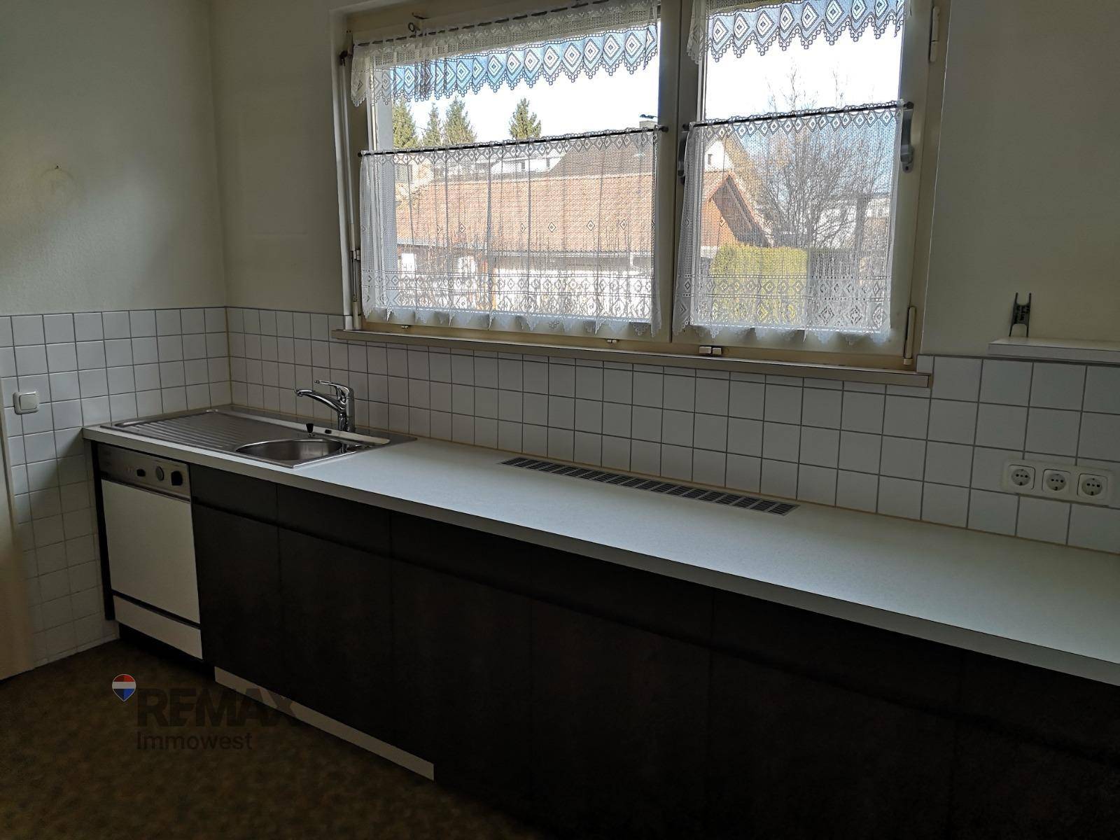 Einfache Küche mit Spüle, Arbeitsplatte und Fenster mit Vorhängen.