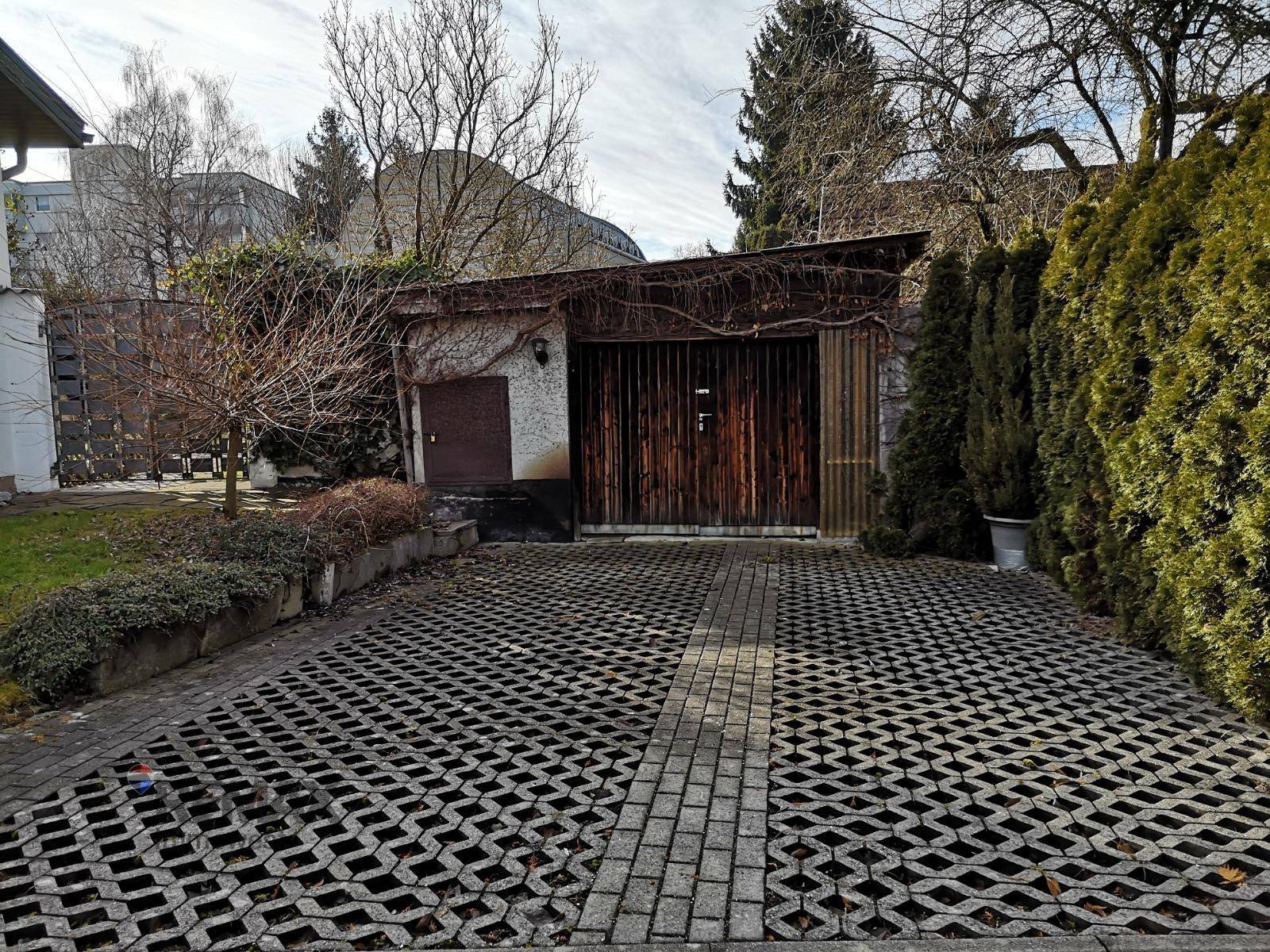 Einfahrt zum Garagengebäude mit Gittersteinen und bewachsenen Mauern.
