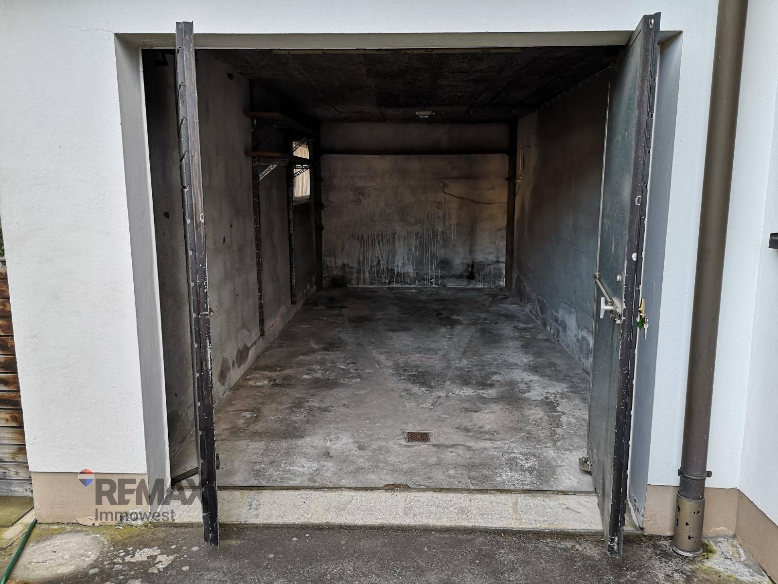 Leere Garage mit Betonboden und geöffneten Metalltoren.
