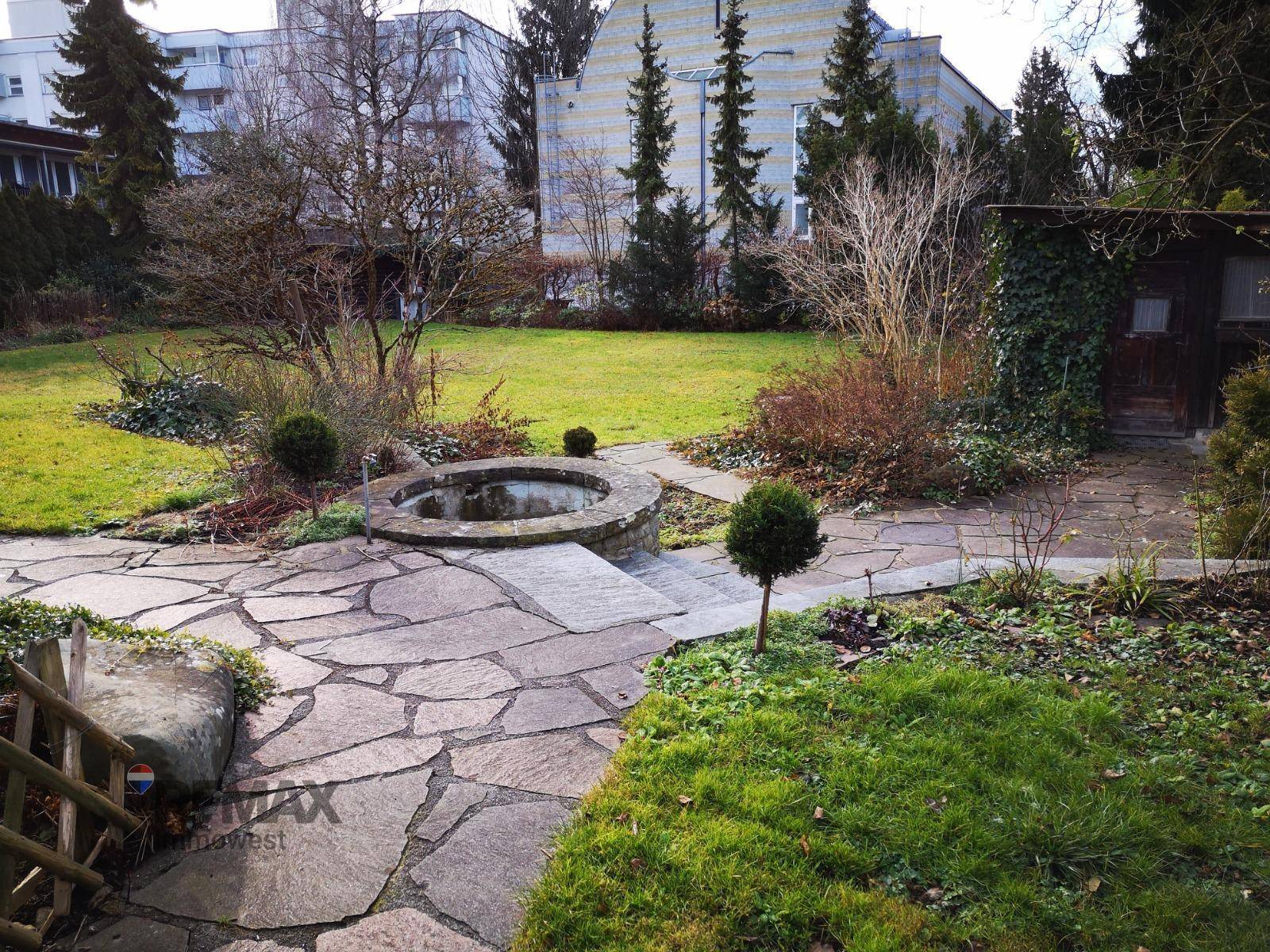 Gartenbereich mit Natursteinwegen, Rasenfläche und einem kleinen Teich oder Brunnen.