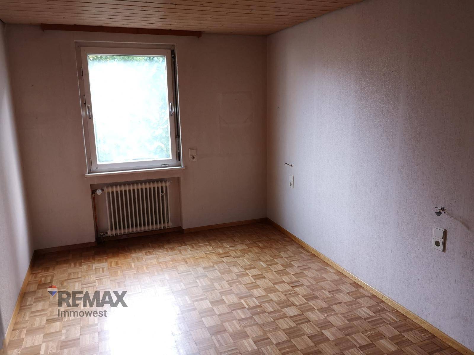 Helles Zimmer mit Parkettboden, Holzdecke und Fenster.