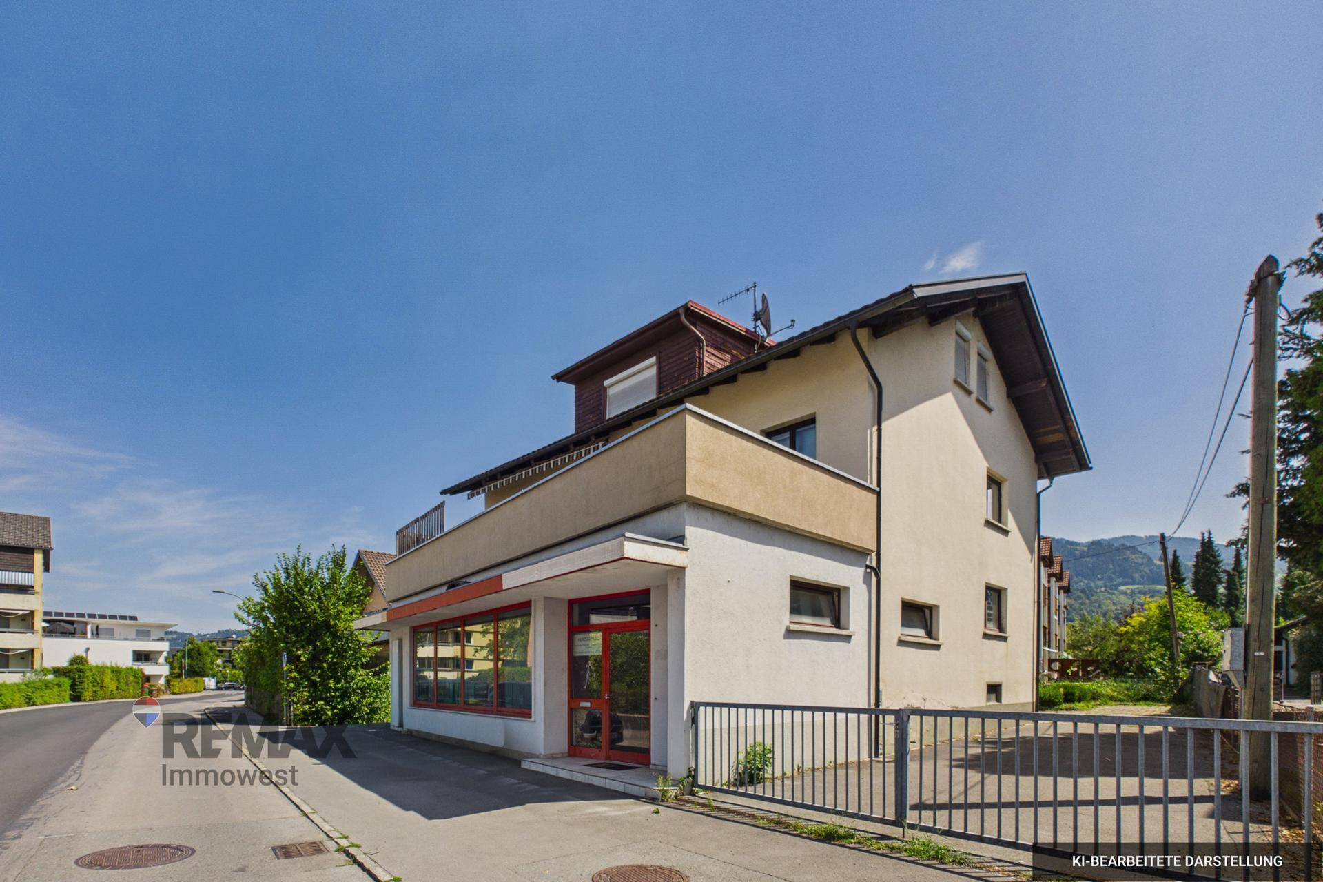 Außenansicht des Gebäudes mit Ladenfront im Erdgeschoss und einer Terrasse im Obergeschoss.