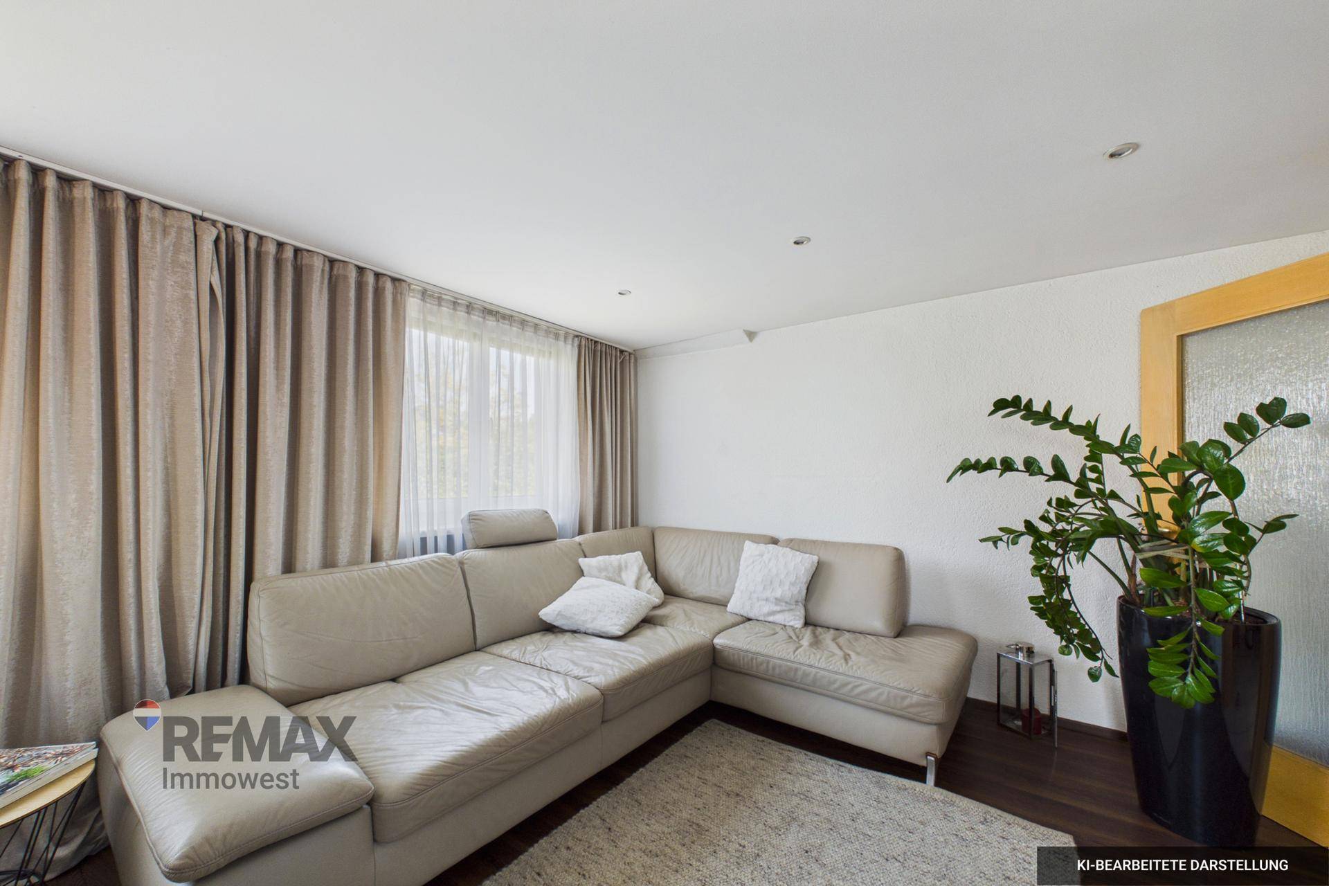 Wohnzimmer mit großem beigem Ecksofa, dunklem Holzboden und einer Zimmerpflanze.