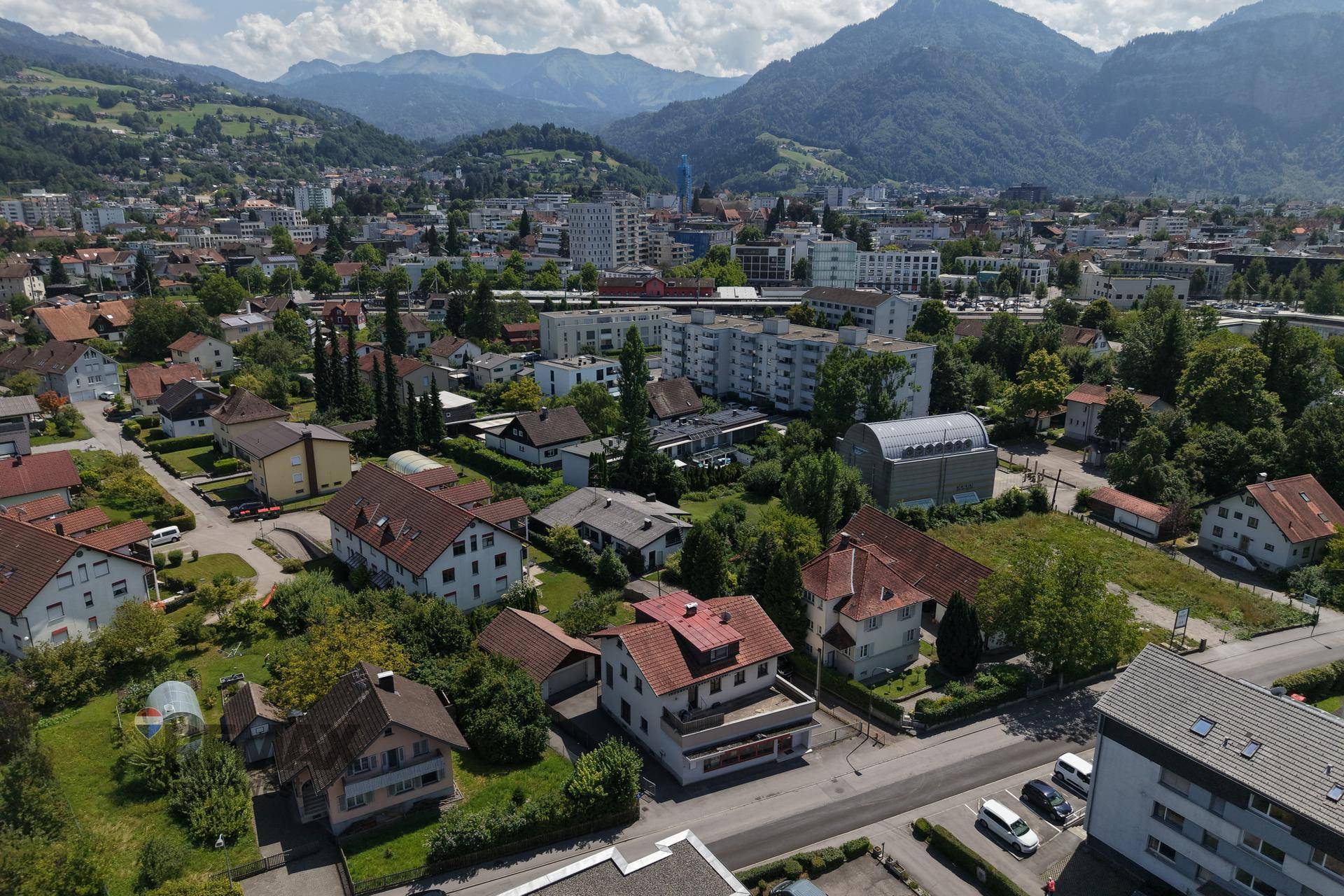 Weitläufige Luftaufnahme einer Stadt mit Wohngebäuden und majestätischen Bergen im Hintergrund.