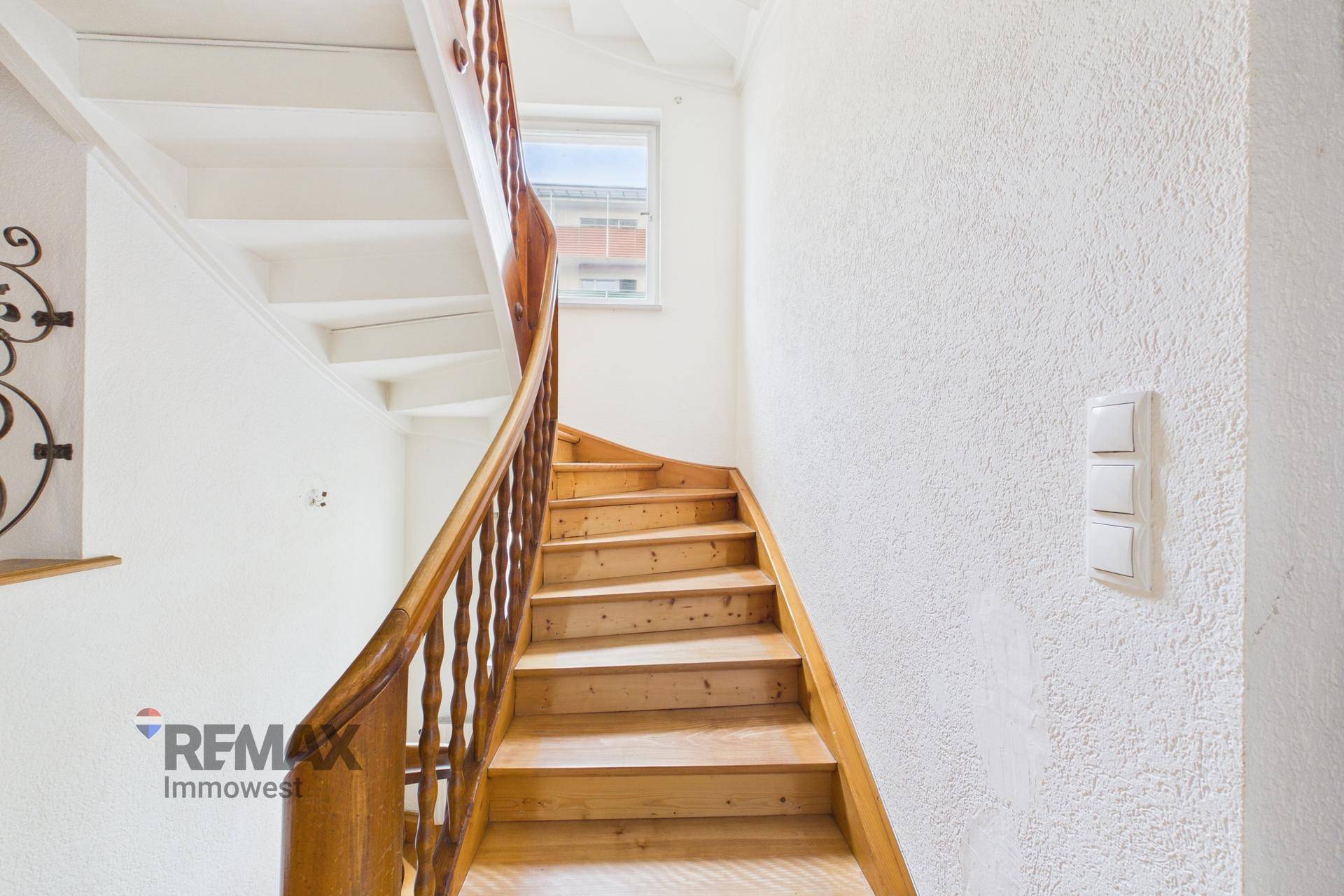 Holztreppe mit geschwungenem Geländer und Fenster, die in die obere Etage führt.