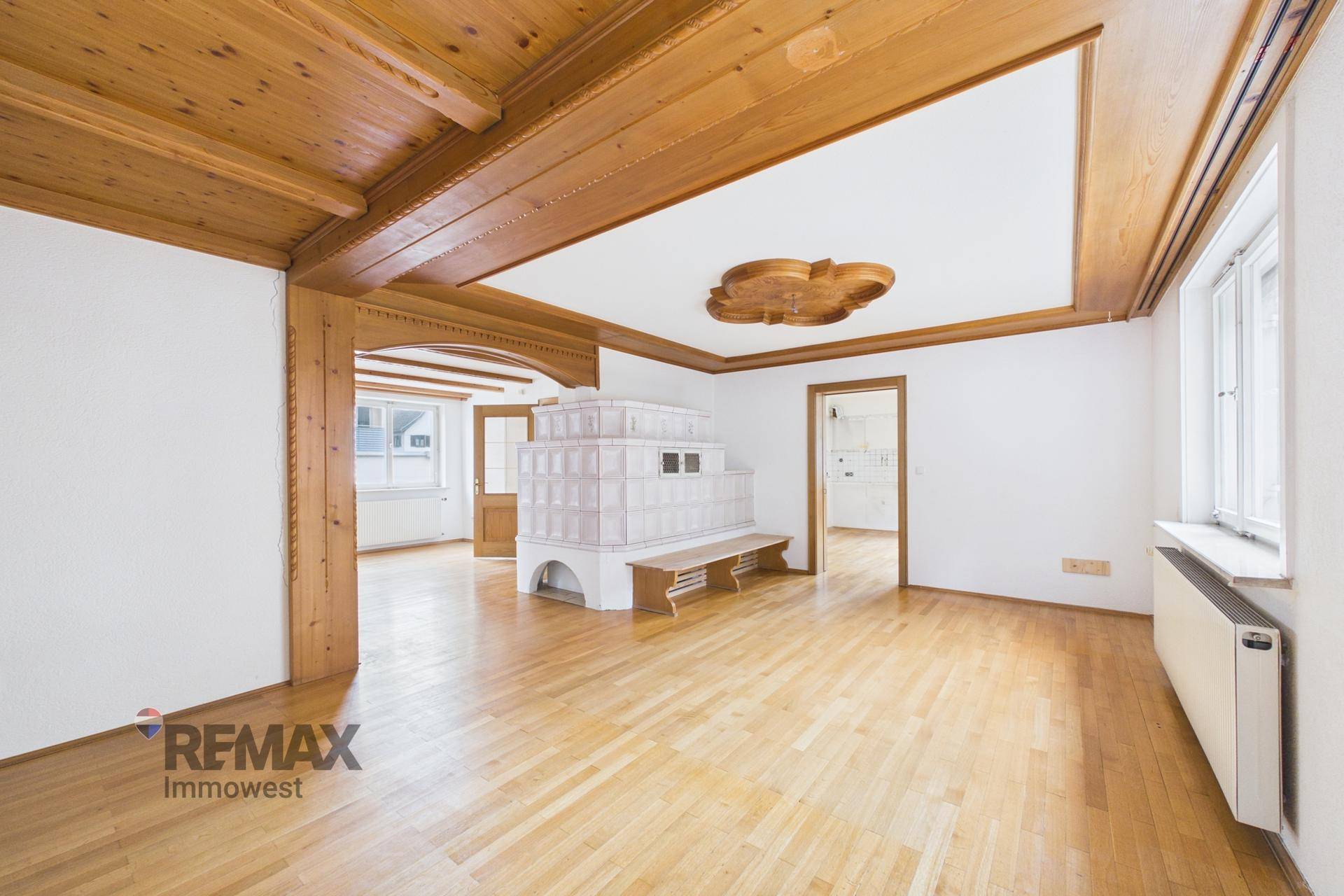 Großes Wohnzimmer mit Holzbalken, Parkettboden und einem traditionellen Kachelofen.