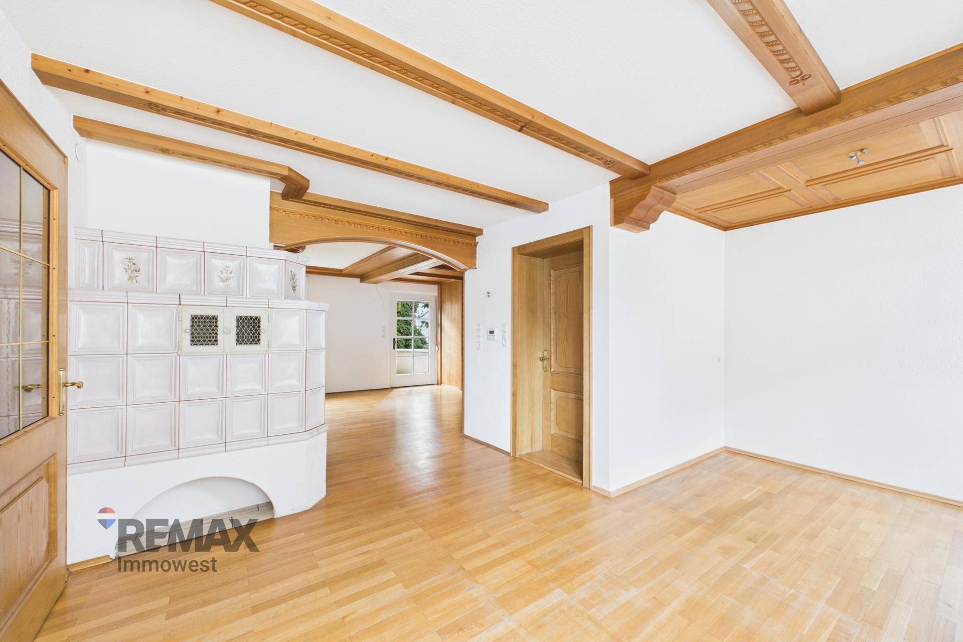 Helles Wohnzimmer mit Holzbalken, Parkettboden und einem traditionellen Kachelofen.