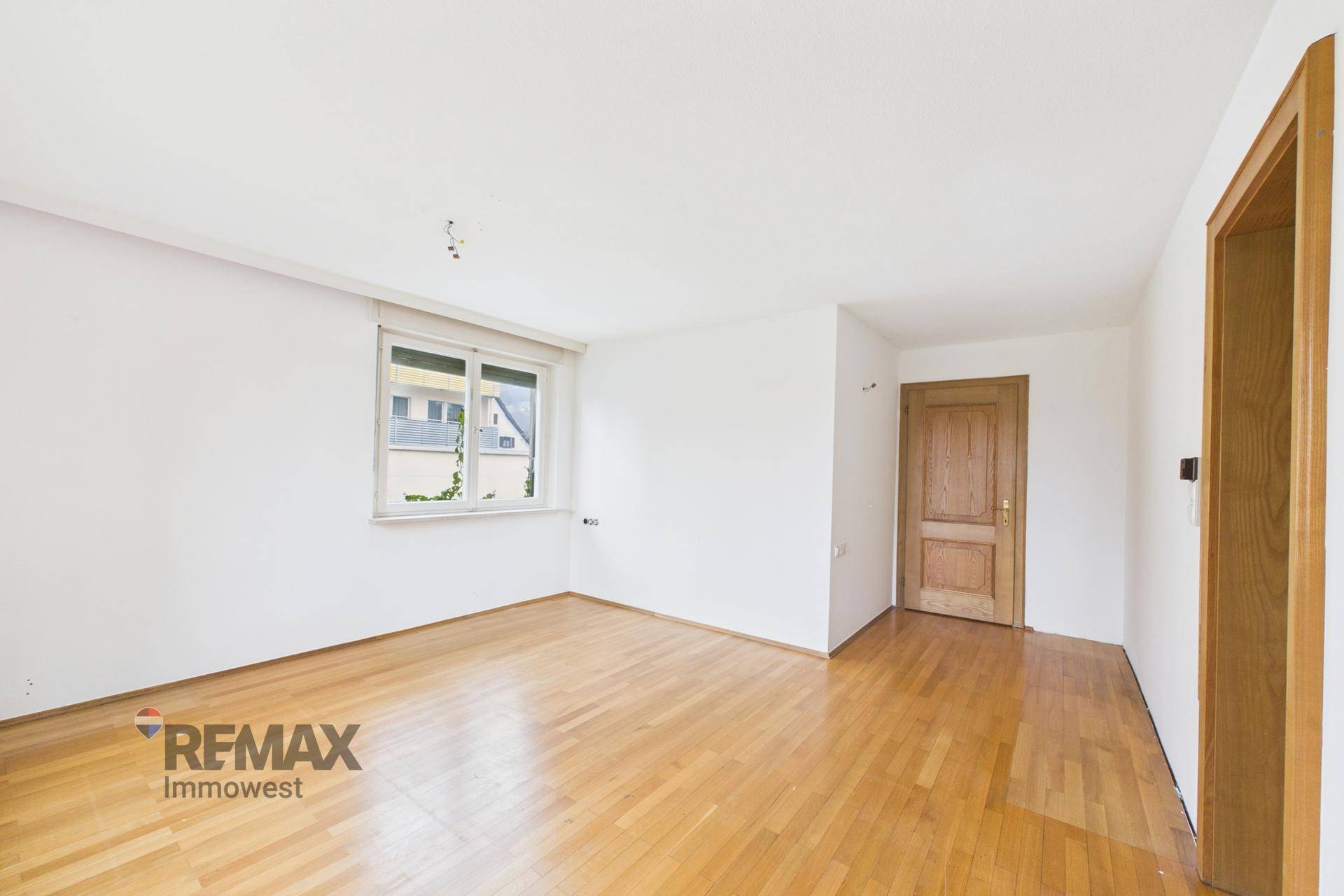 Helles Schlafzimmer mit Parkettboden und einem Fenster, das den Raum erhellt.