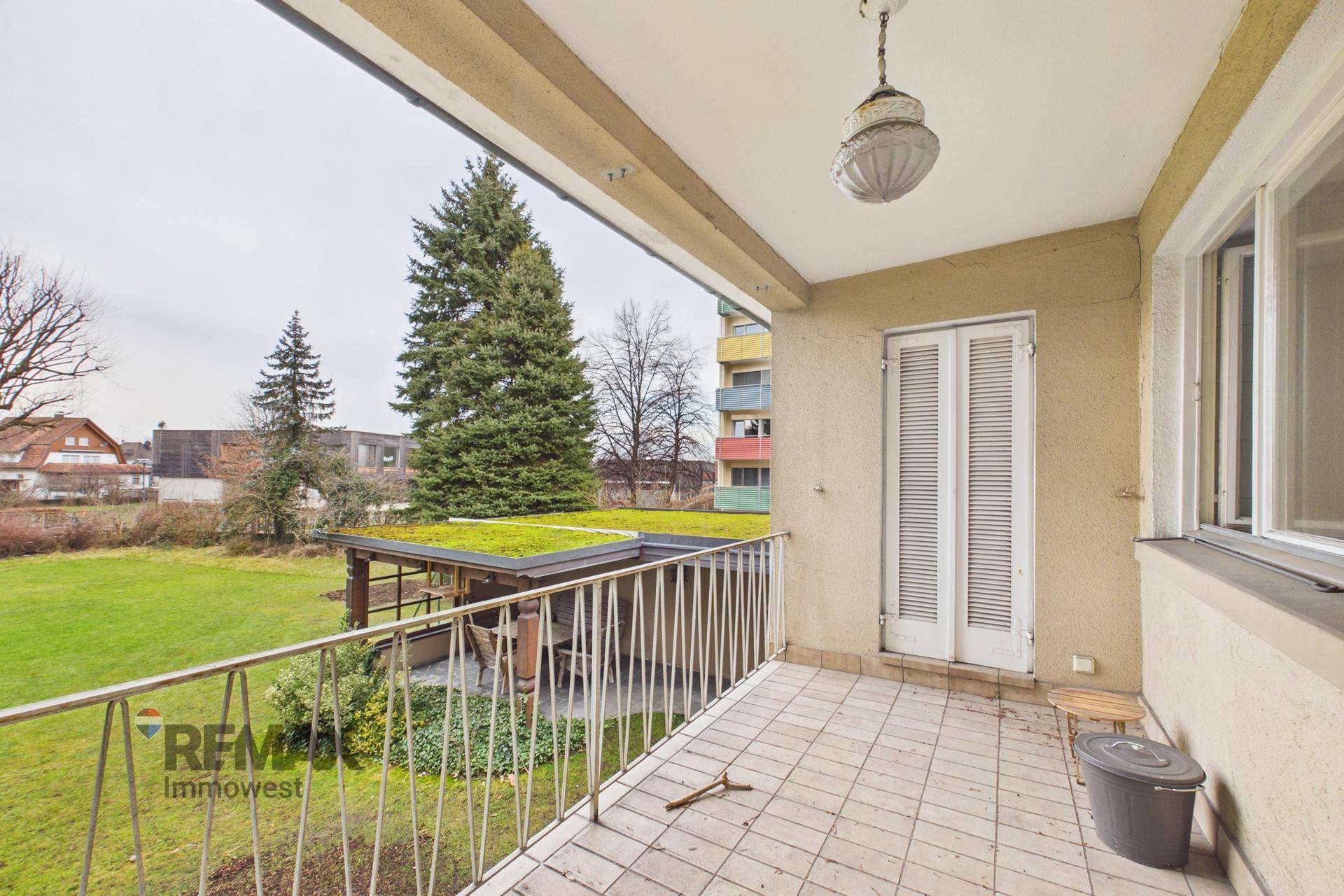 Balkon mit Fliesenboden und Metallgeländer, Blick auf den Garten und umliegende Gebäude.